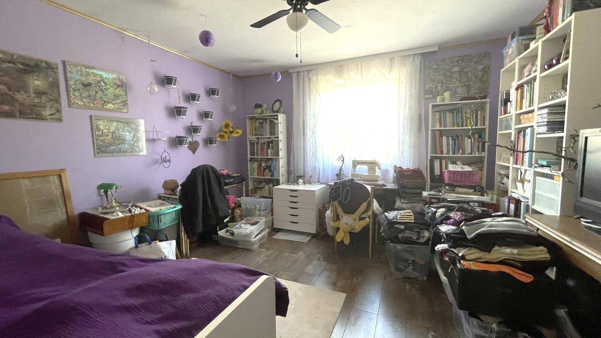 Schlafzimmer mit lila Wänden, Bücherregalen und einem Deckenventilator.