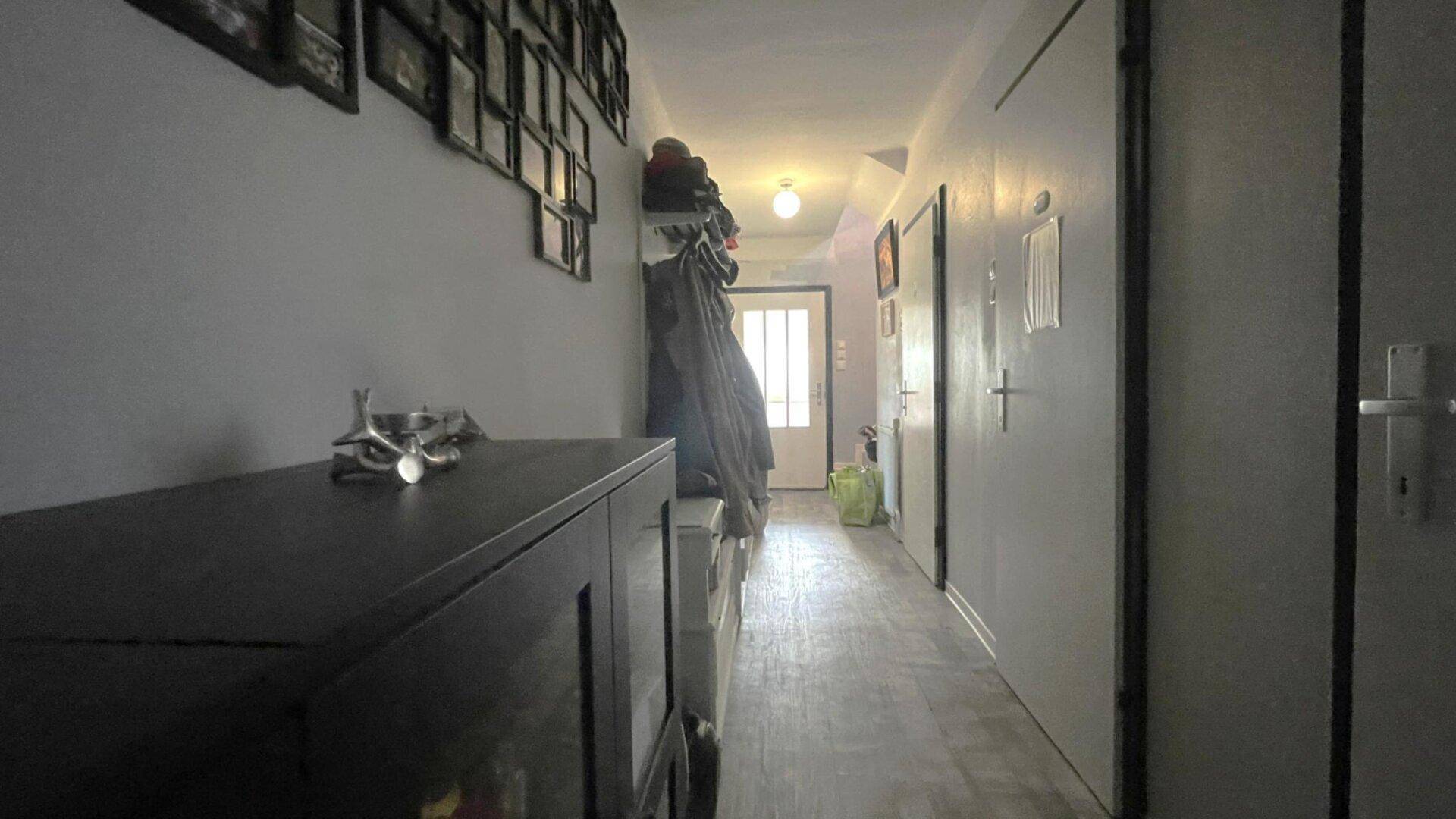 Langer Flur mit dunklem Boden, vielen Türen und Bildern an der Wand.