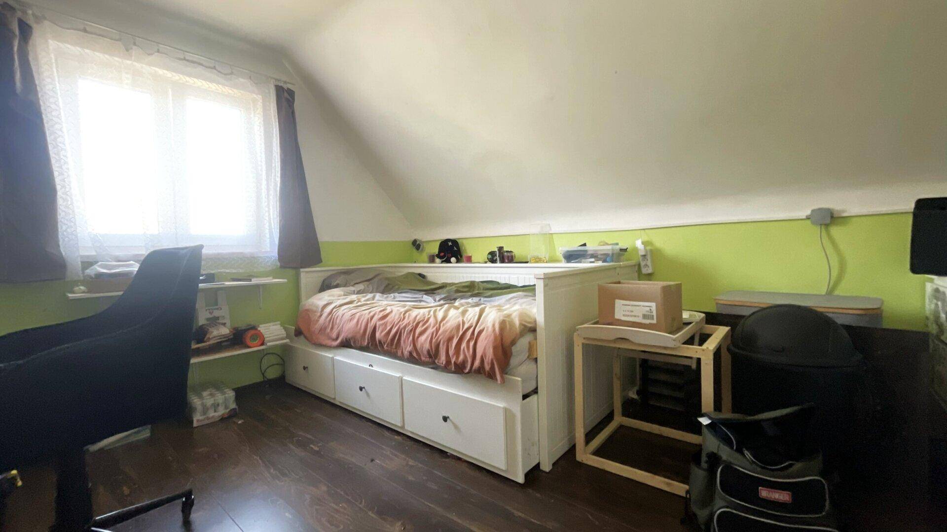 Schlafzimmer im Dachgeschoss mit schrägen Wänden, grünem Akzent und Fenster.
