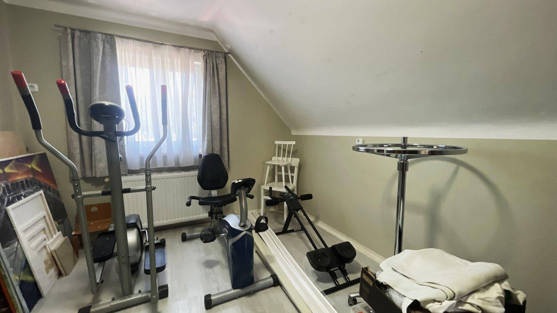 Dachgeschossraum mit verschiedenen Fitnessgeräten und schrägen Wänden, ideal für ein Heim-Fitnessstudio.