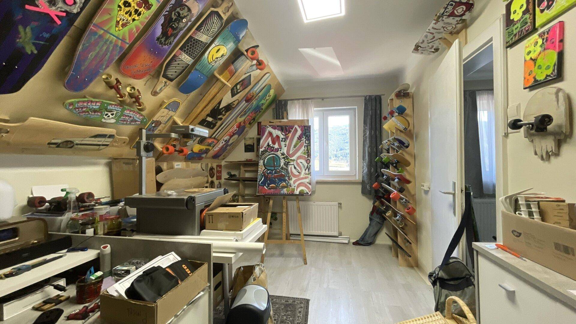 Kreativer Arbeitsraum im Dachgeschoss mit vielen Skateboards an den Wänden und einem Fenster.