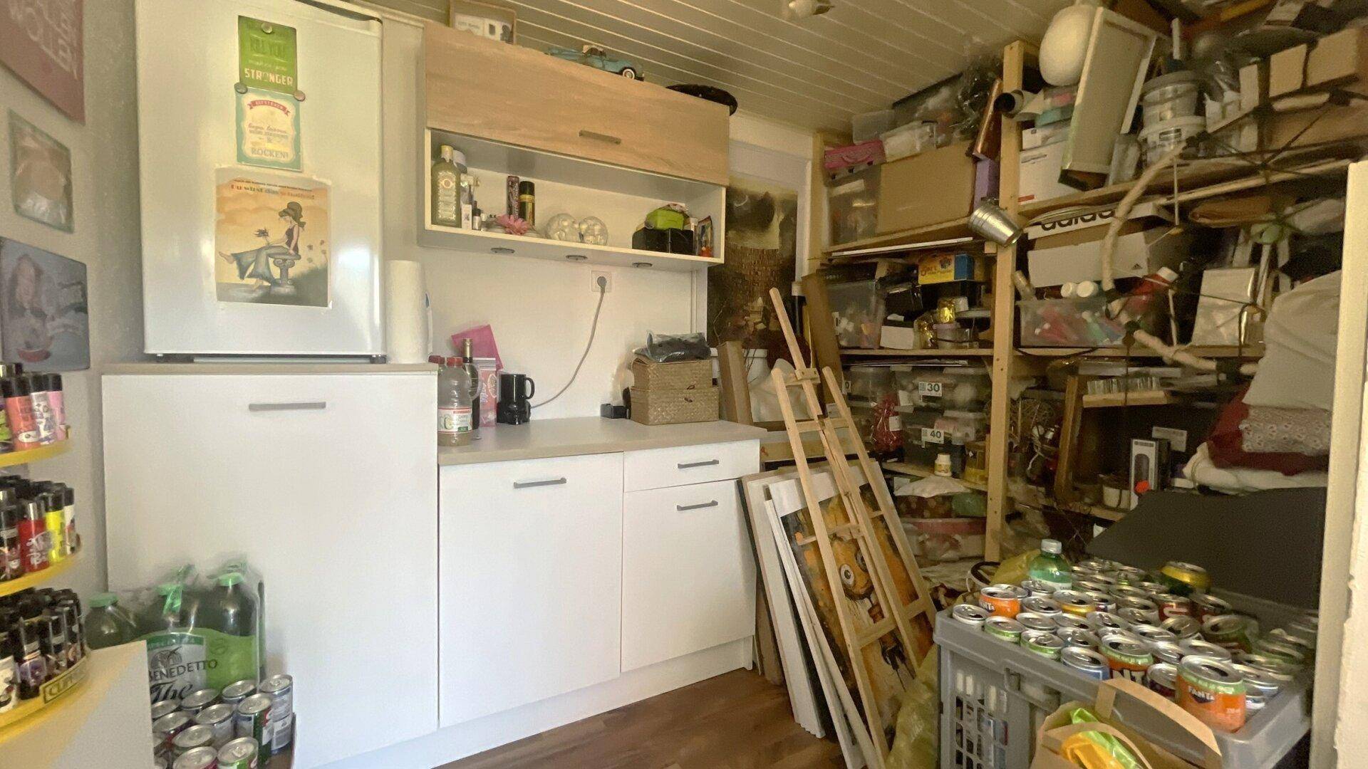 Abstellraum mit kleiner Küchenzeile, Kühlschrank und vielen Vorräten und Lagerregalen.
