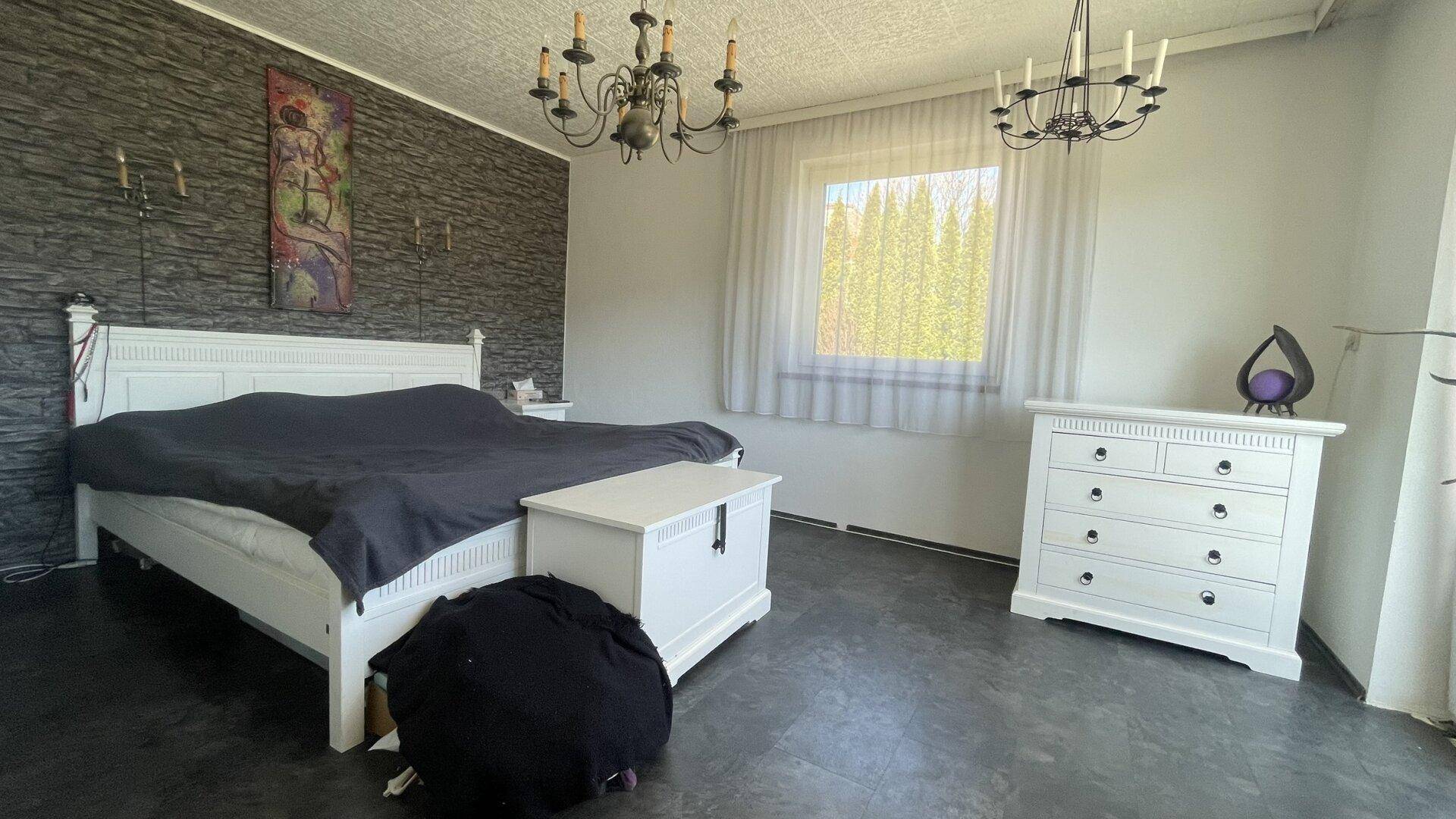 Schlafzimmer mit dunklem Boden, weißem Bett und Kommode, sowie einer strukturierten Wand.