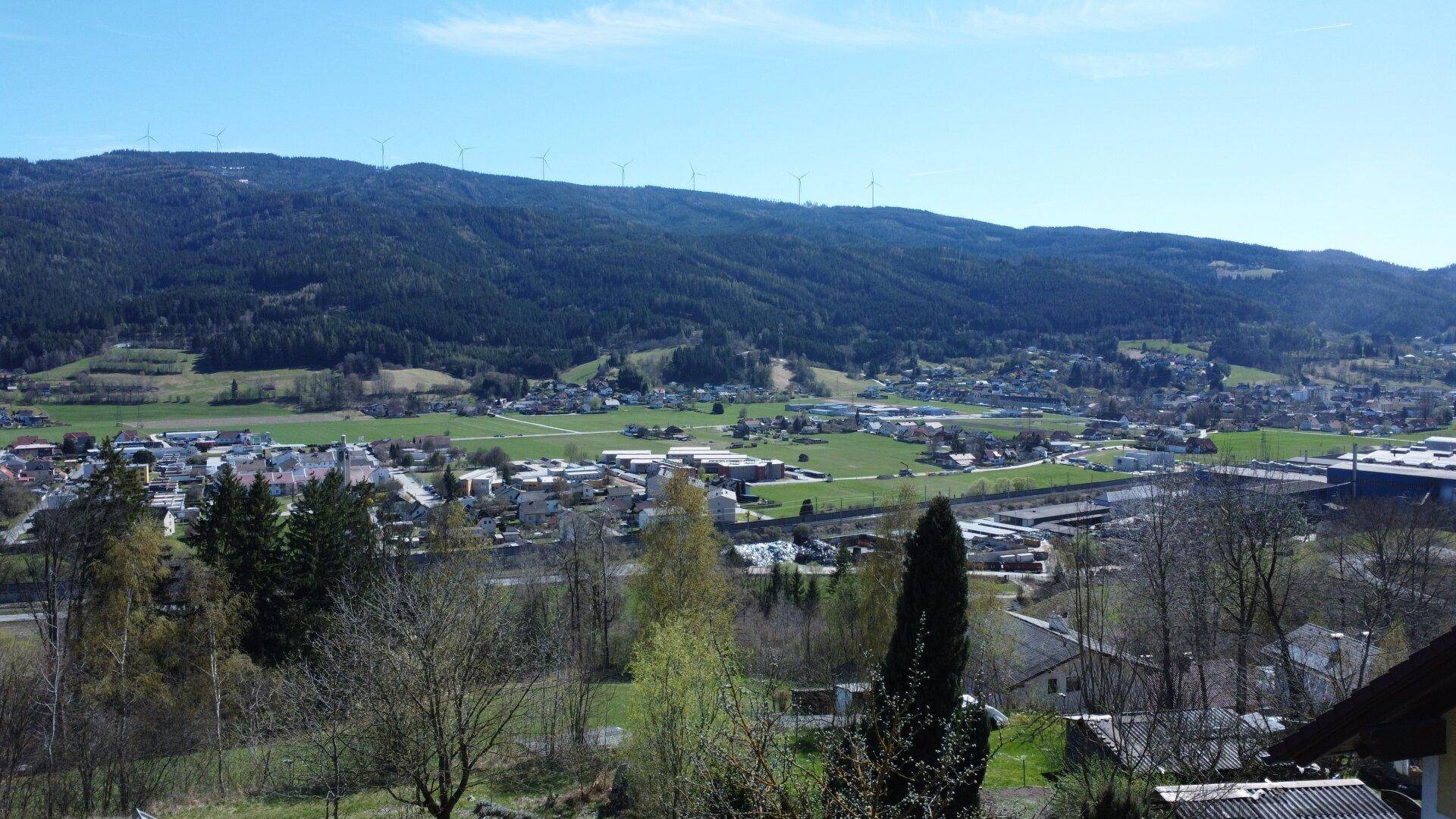 Weitläufiger Blick über die Landschaft mit einer Stadt und Windrädern am Horizont.