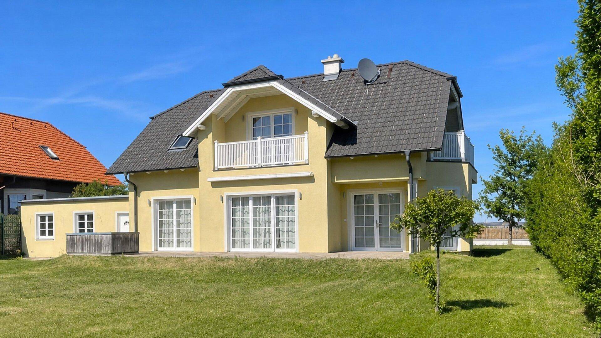 Attraktives gelbes Einfamilienhaus mit dunklem Dach und gepflegtem Rasen im Gartenbereich.