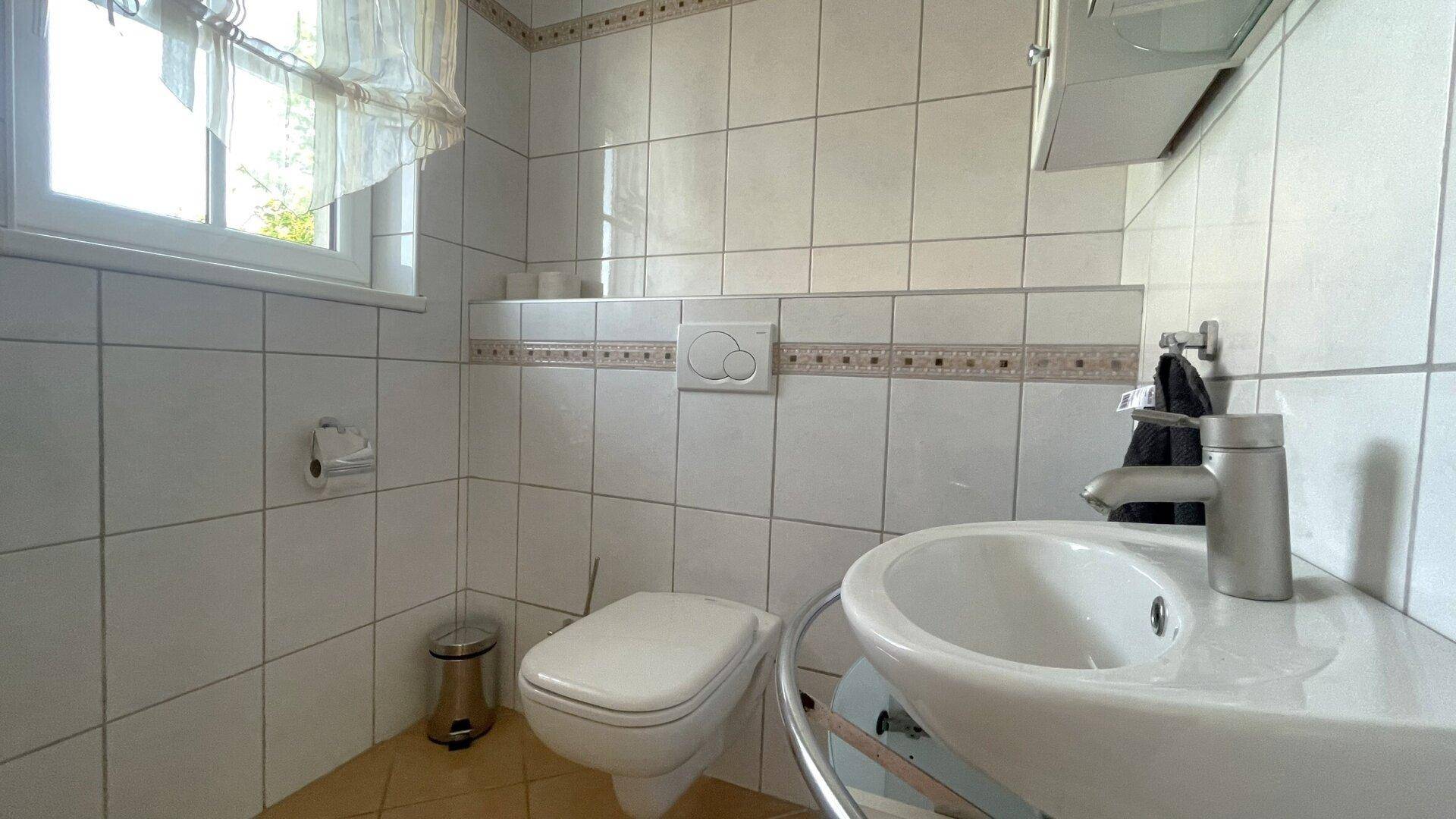 Kleines Gäste-WC mit Toilette, Waschbecken und Fenster, komplett gefliest.