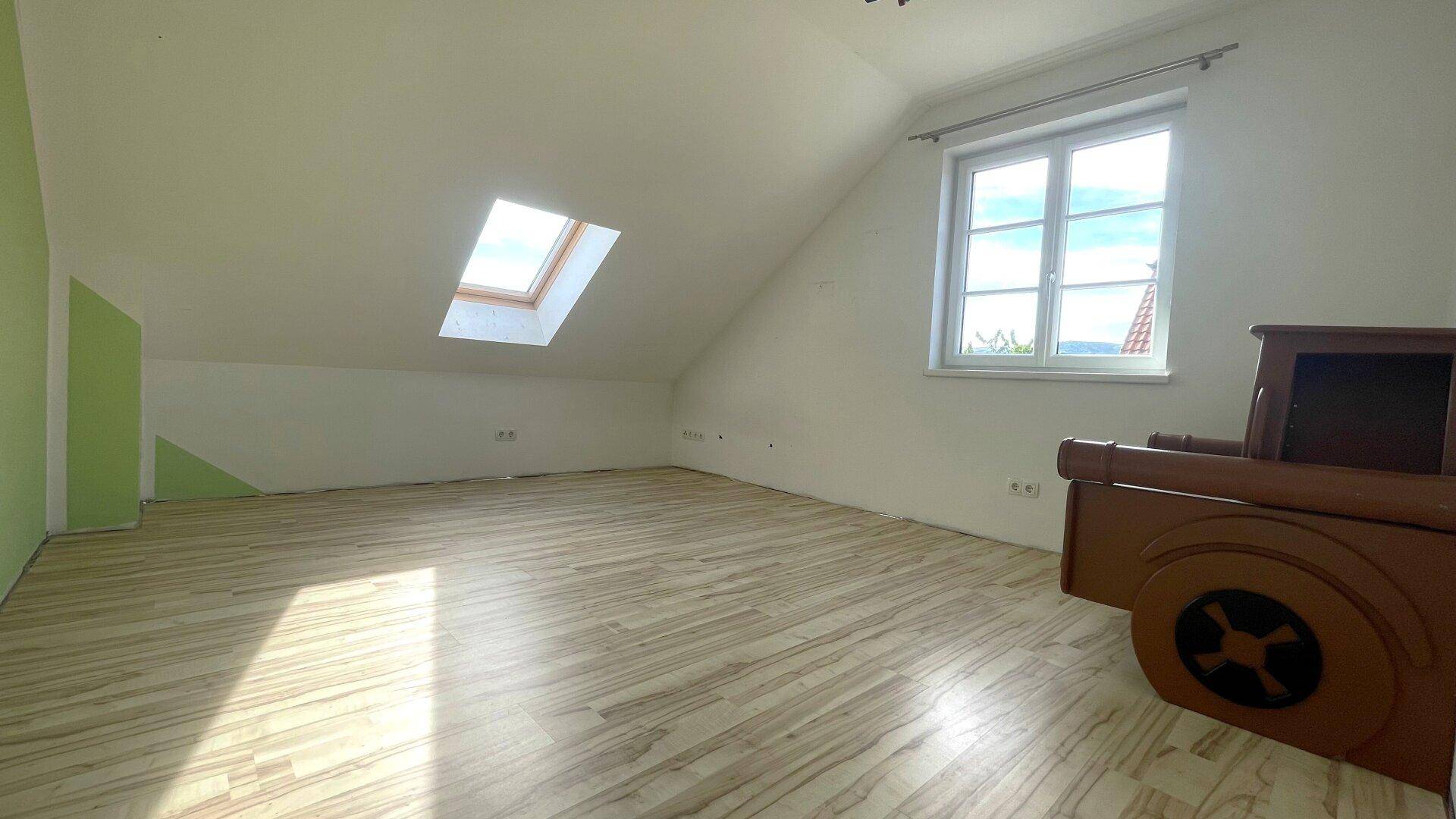 Geräumiger Raum mit hellem Laminatboden, Dachfenster und einem kleinen Möbelstück.