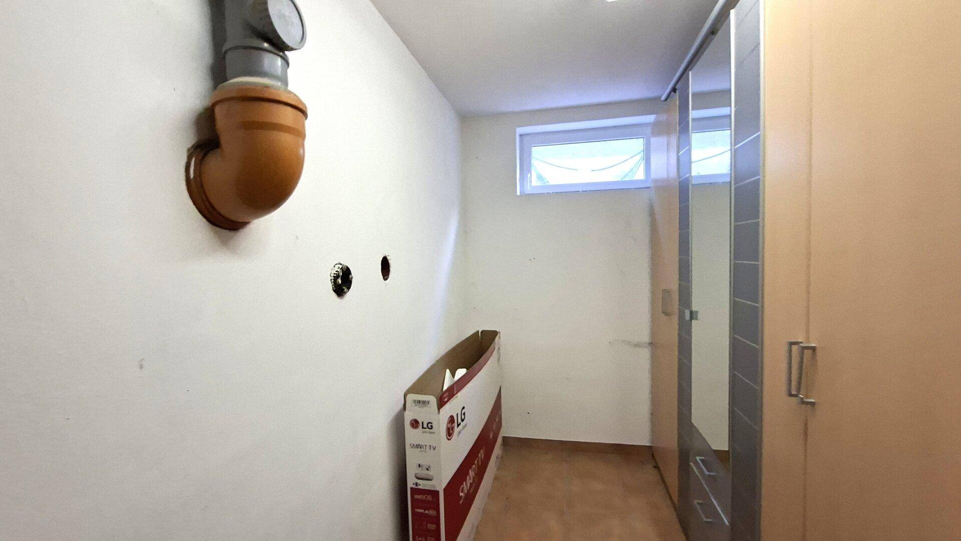 Abstellraum mit sichtbaren Rohren, einem Fenster und einem Schrank für zusätzlichen Stauraum.