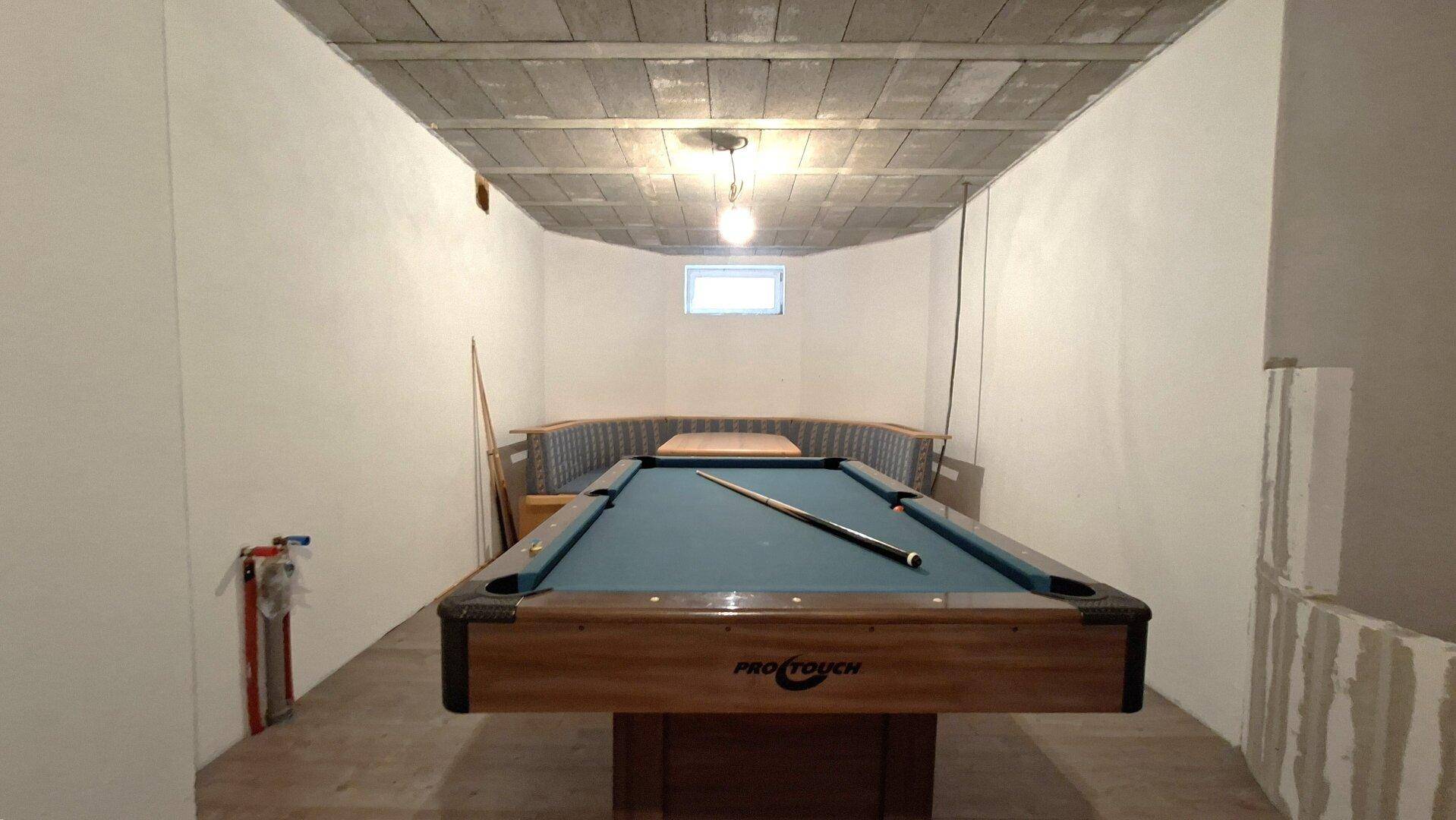 Unterhaltungsraum im Keller mit Billardtisch, Sitzgelegenheiten und einem kleinen Fenster.