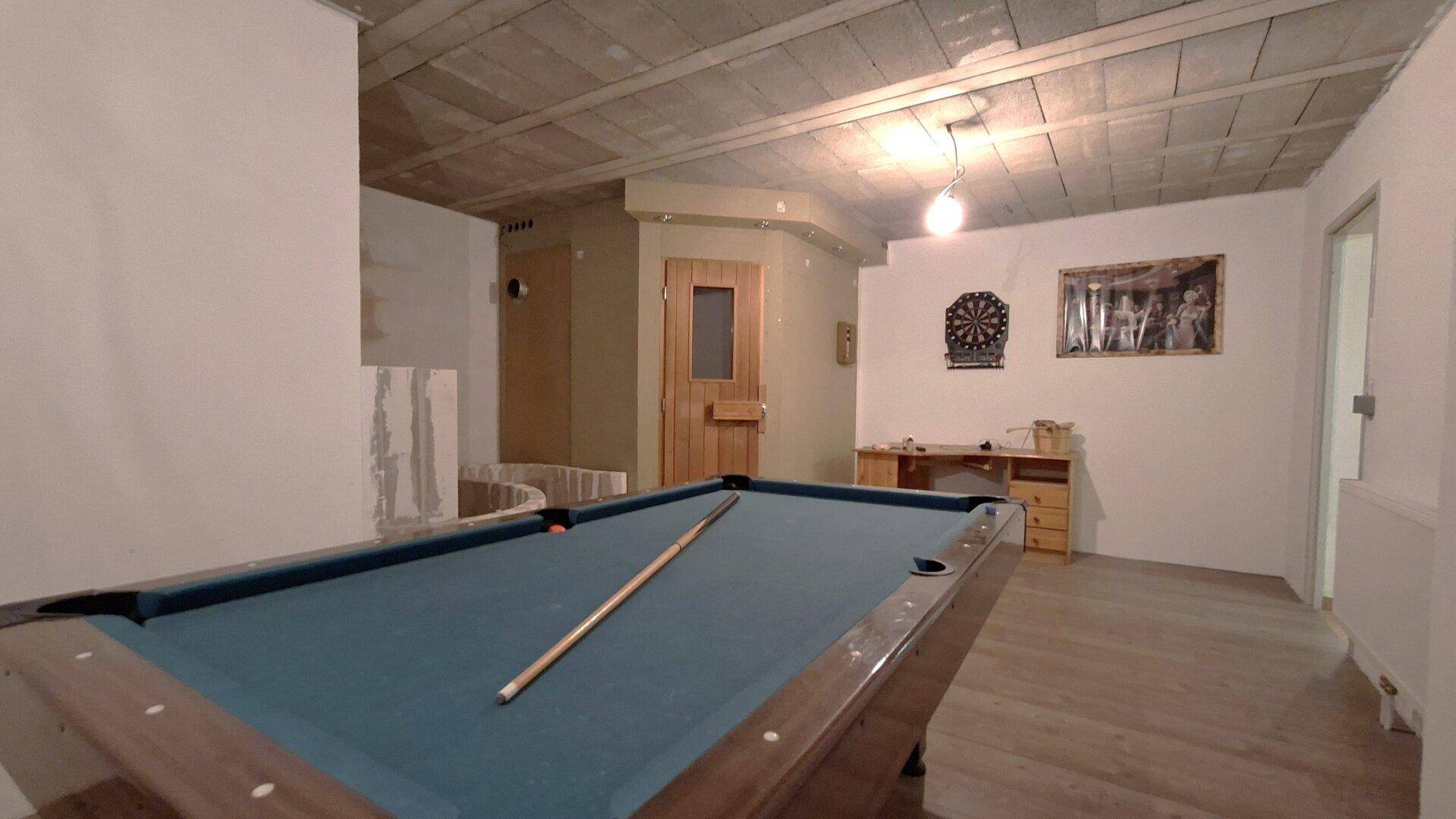 Kellerraum mit Billardtisch, Dartscheibe und einer sichtbaren Sauna im Hintergrund.