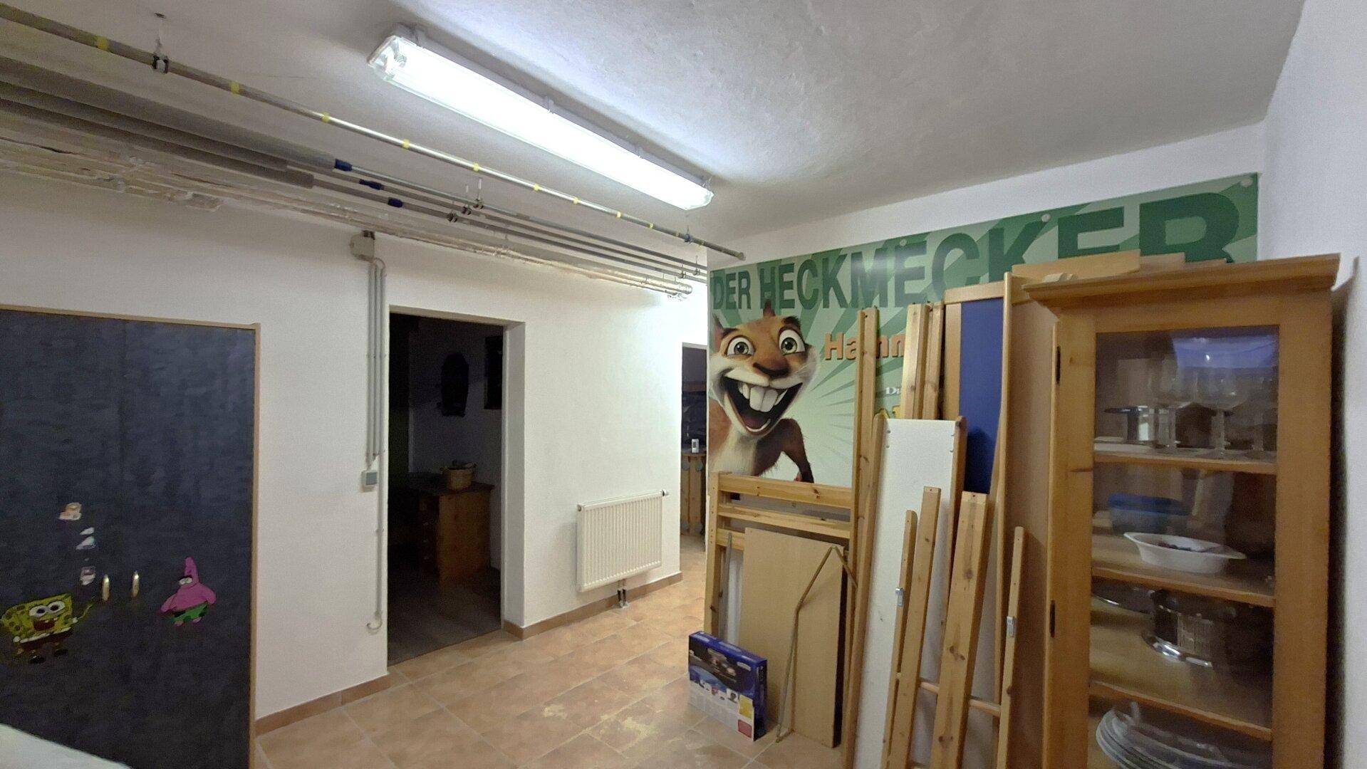 Unfertiger Kellerraum mit Wandgrafik, Lagergegenständen und einfacher Beleuchtung.
