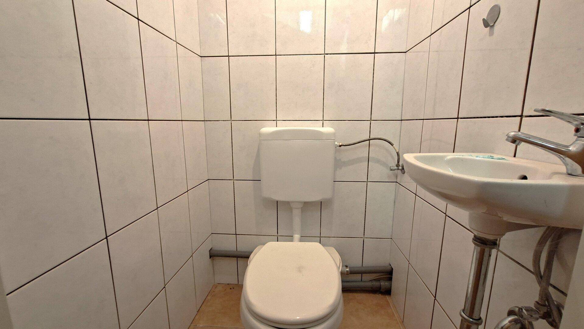 Kleines WC mit Toilette und wandmontiertem Waschbecken, vollständig gefliest.