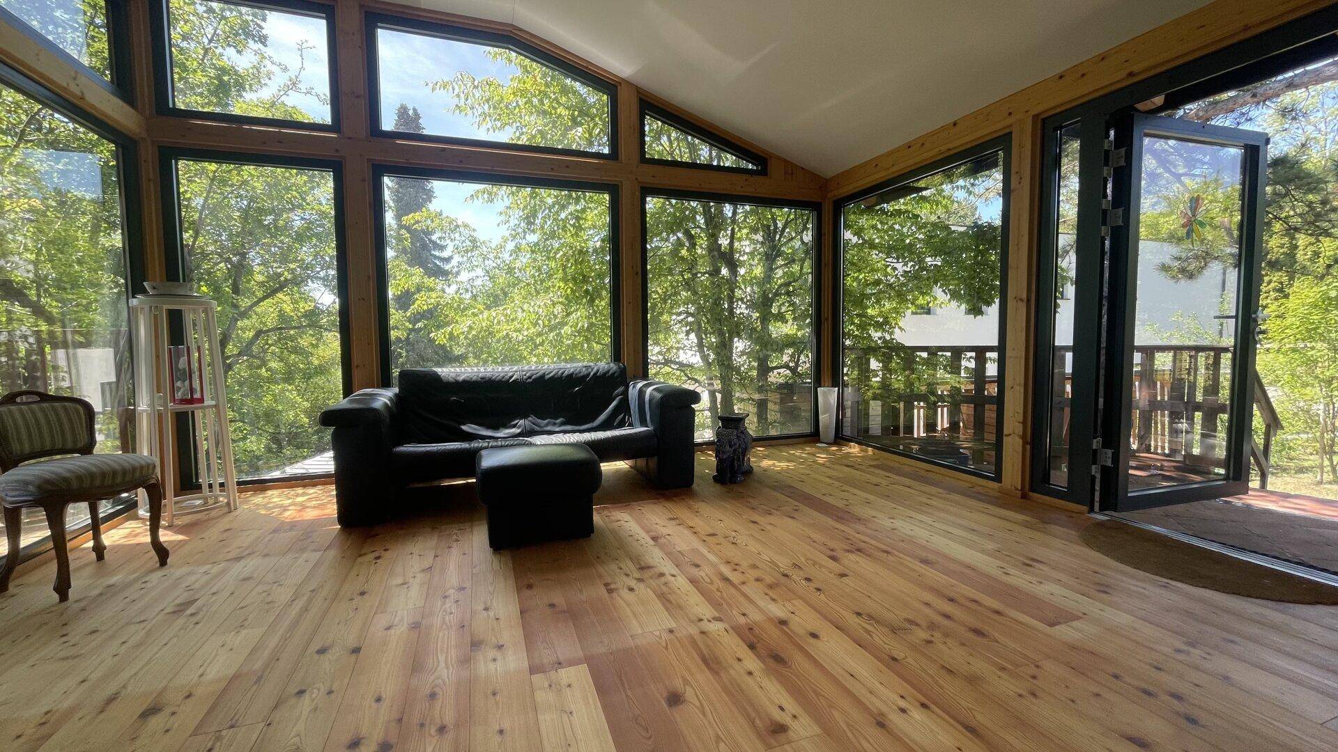 Lichtdurchfluteter Wohnbereich mit Holzboden und großen Panoramafenstern zur Natur.