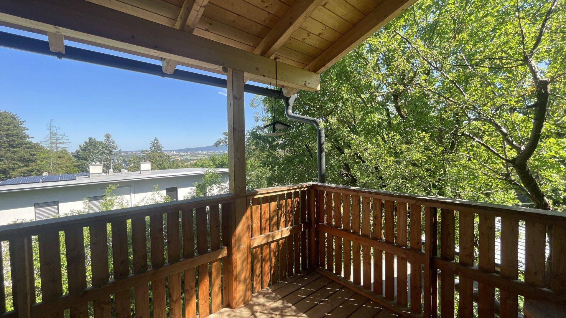 Hölzerner Balkon mit Blick auf die Stadt und die grüne Umgebung unter blauem Himmel.