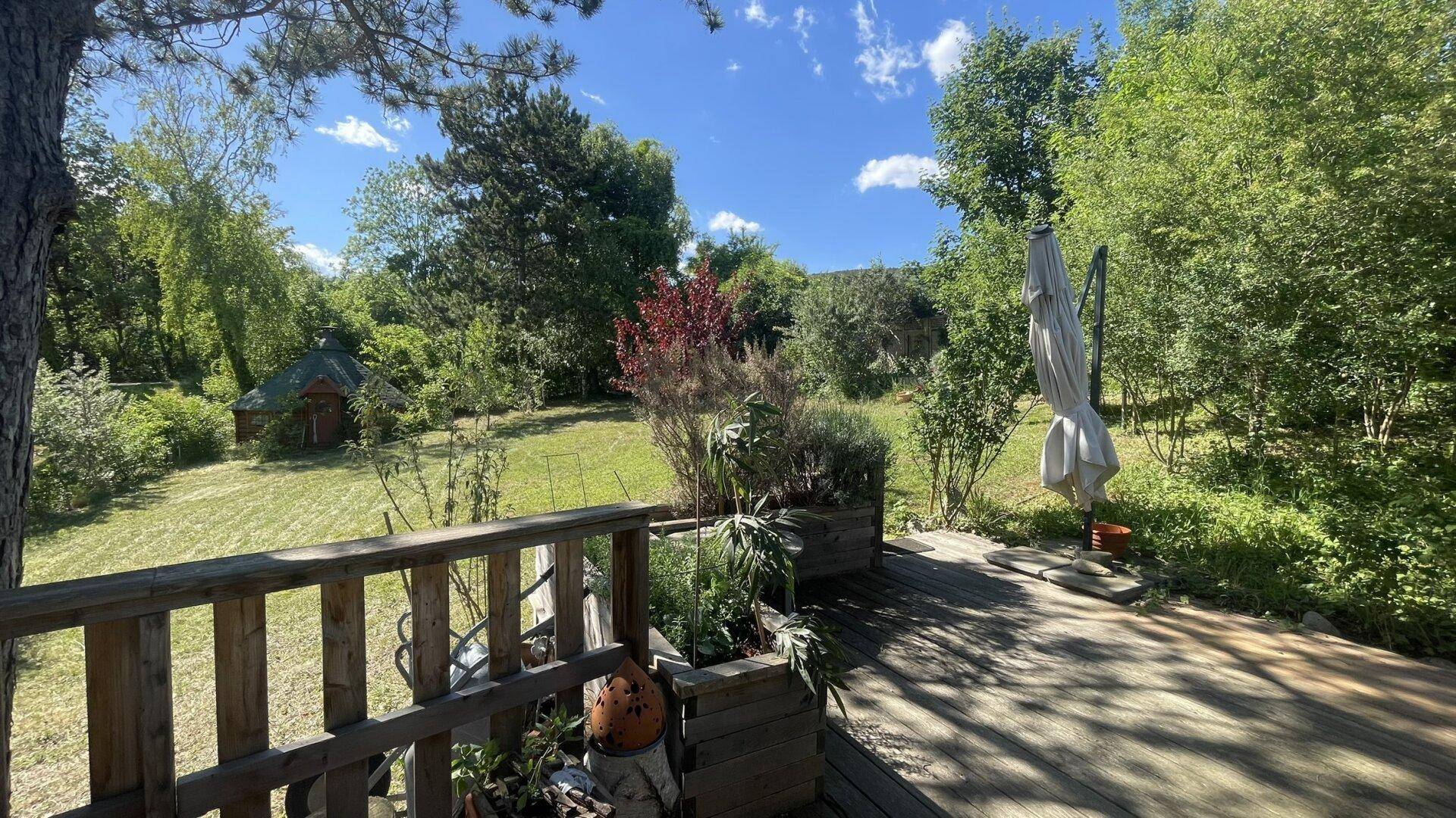 Holzterrasse mit Pflanzen und weitem Blick über den grünen Garten an einem sonnigen Tag.
