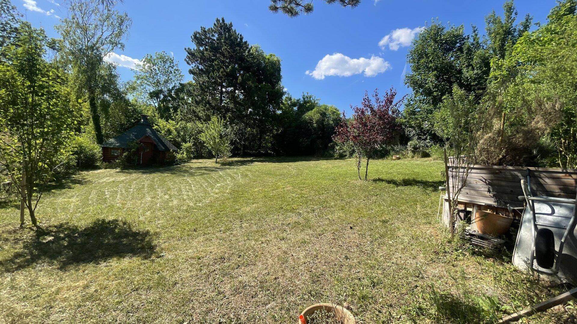Weitläufiger, gepflegter Garten mit großer Rasenfläche und Bäumen unter blauem Himmel.