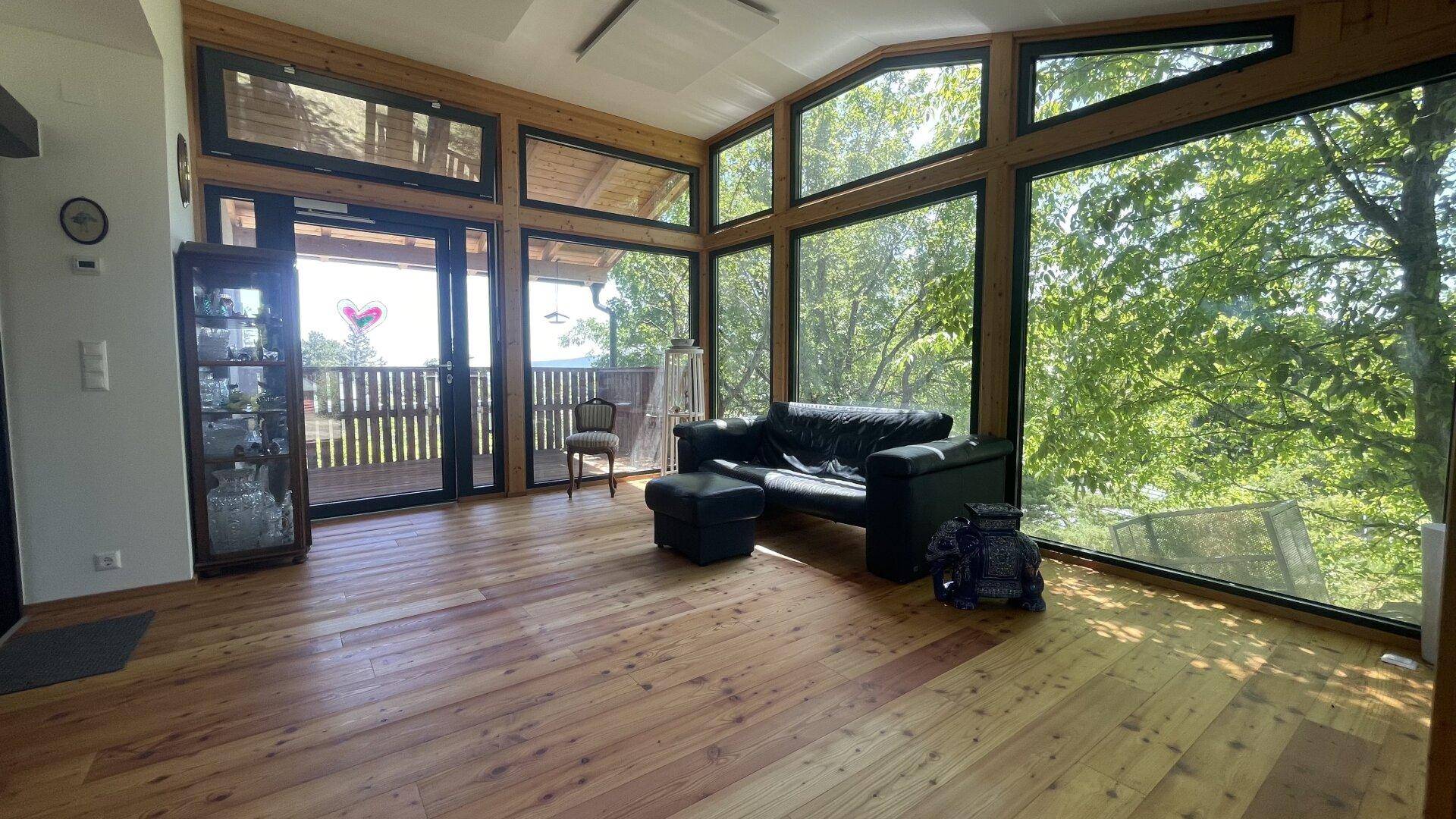 Geräumiger Wohnbereich mit Holzboden, großen Fenstern und Zugang zum Balkon.