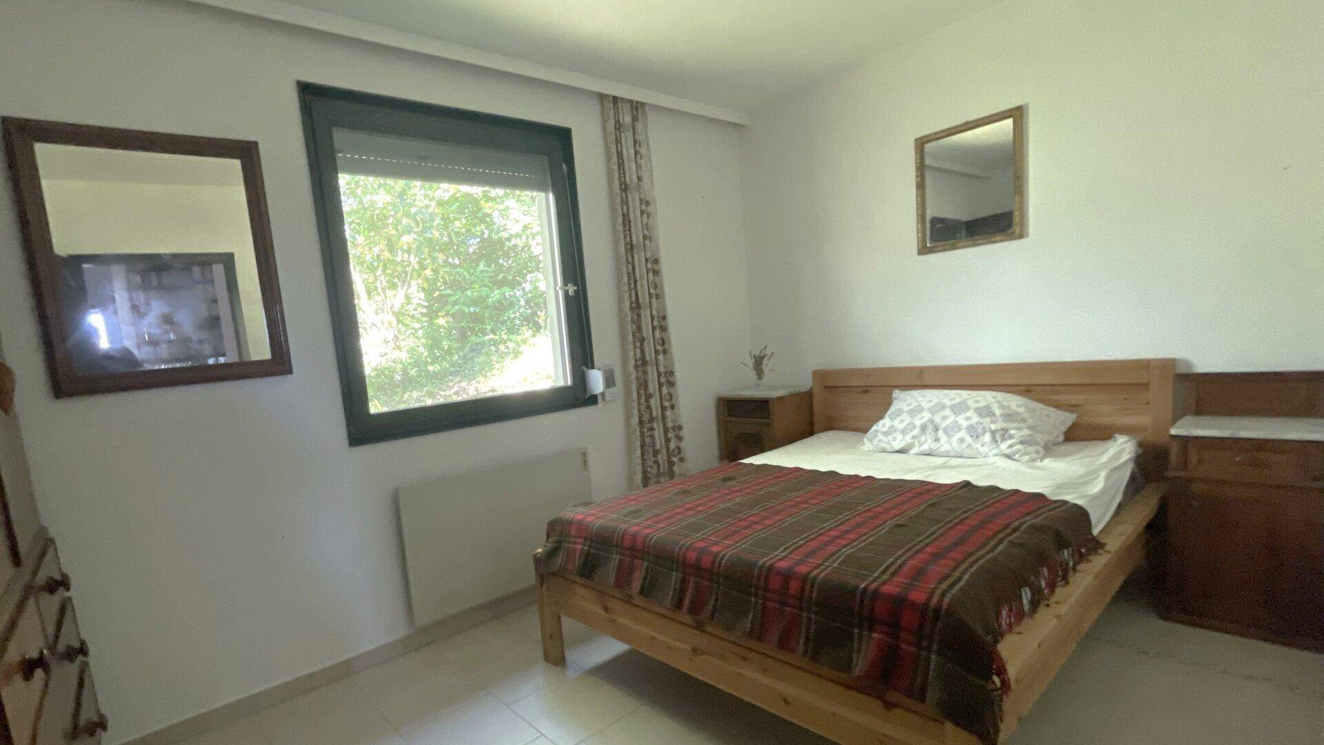 Helles Schlafzimmer mit Holzbett, Fliesenboden und Fenster mit Blick ins Grüne.