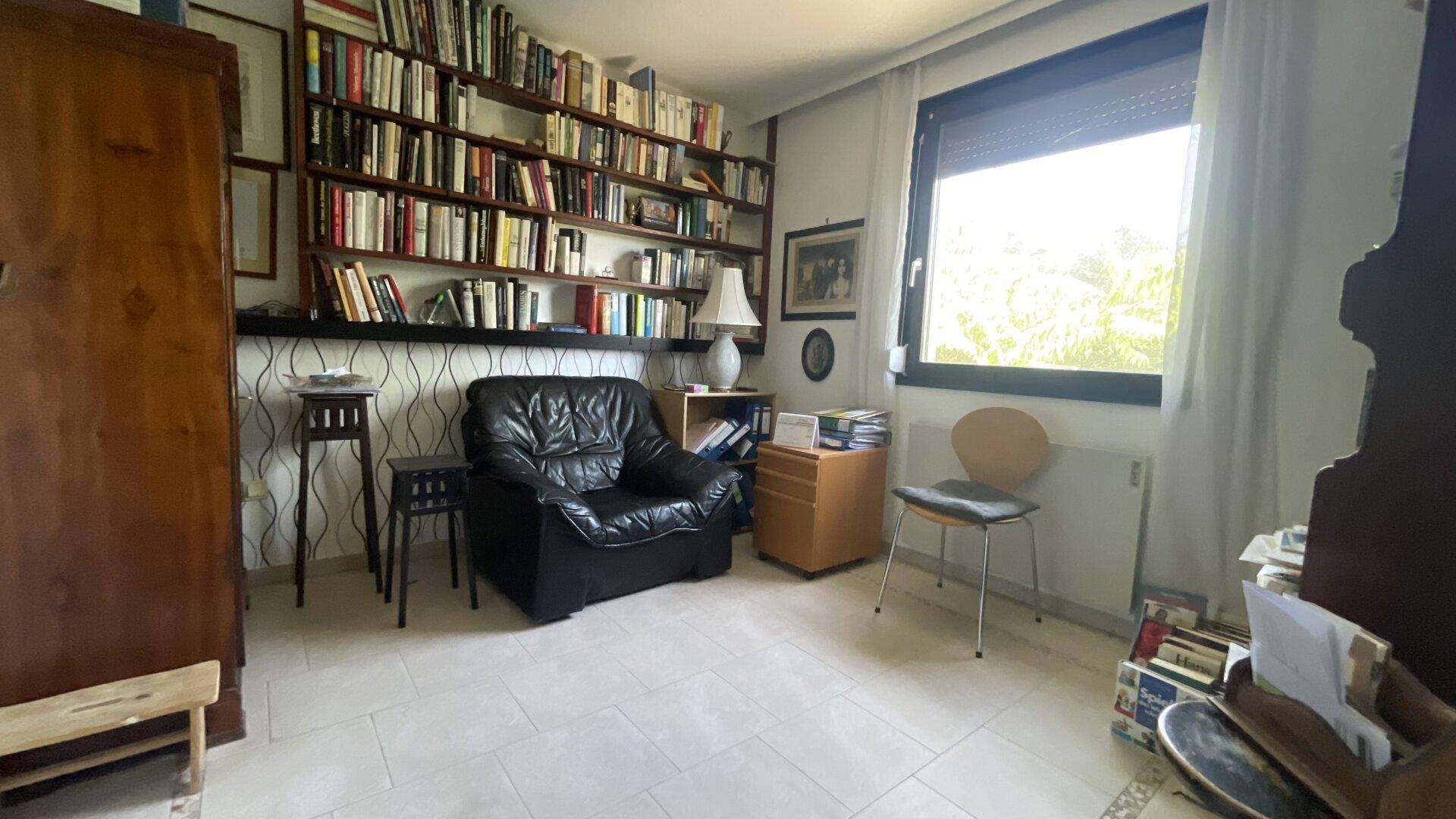 Arbeitszimmer mit Bücherregal, Fliesenboden und großem Fenster für viel natürliches Licht.