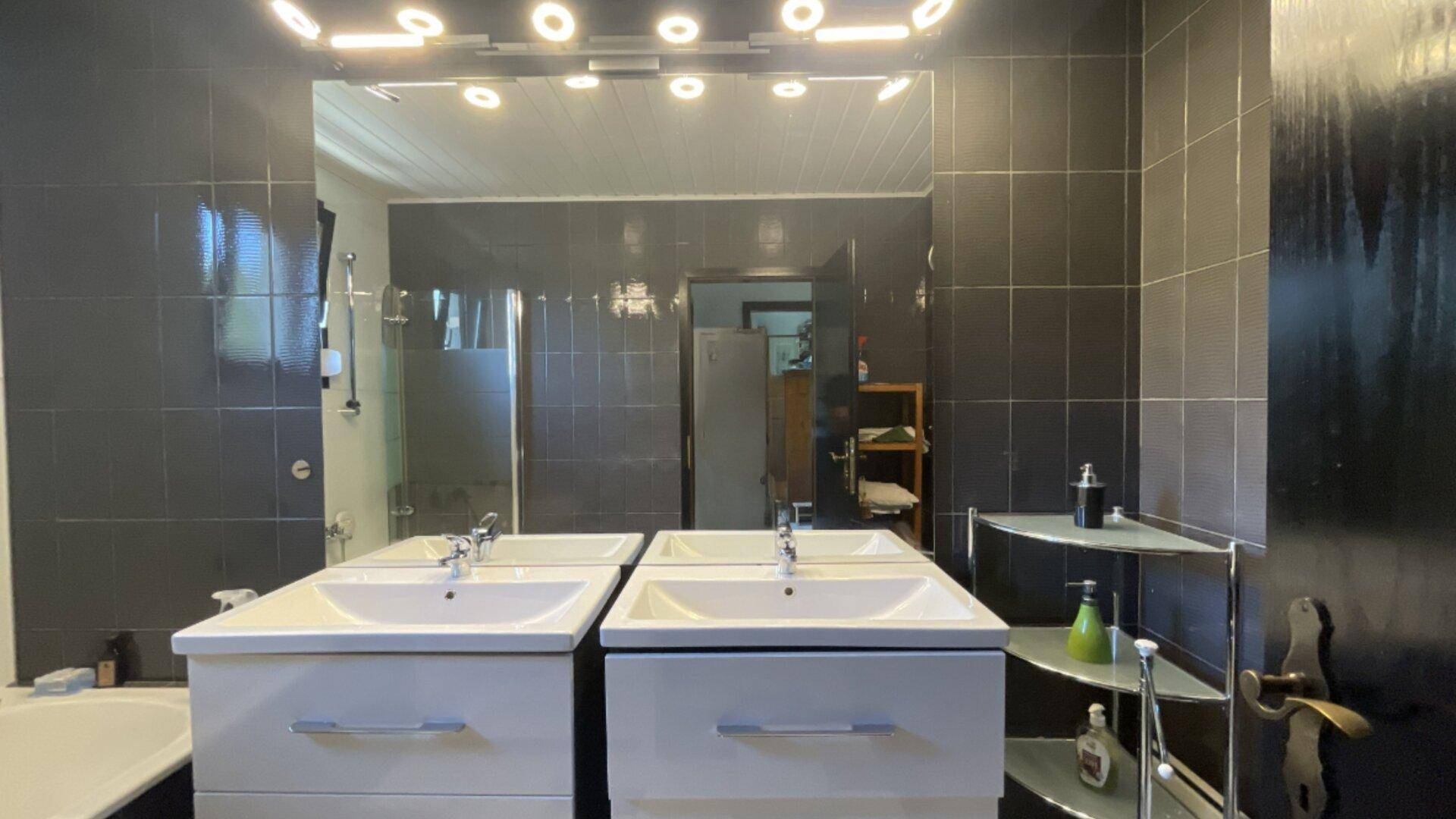 Modernes Badezimmer mit Doppelwaschbecken, großem Spiegel und dunklen Fliesen.