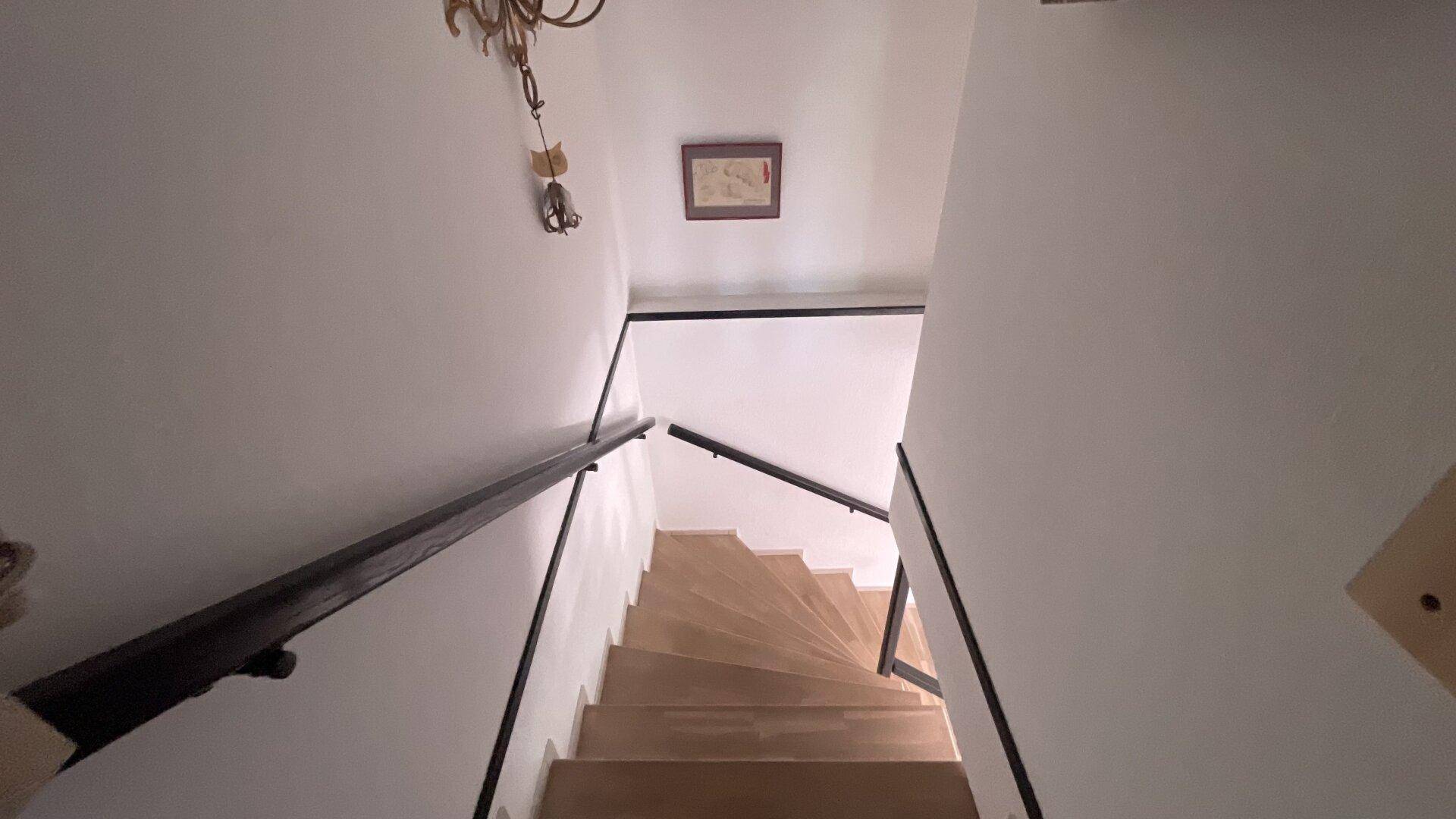 Helle Holztreppe mit schwarzem Geländer, die die Stockwerke des Hauses verbindet.