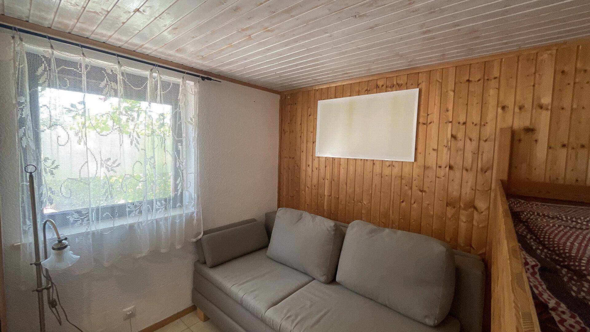 Kleines Schlafzimmer mit Holzvertäfelung, Sofa und Fenster für natürliches Licht.