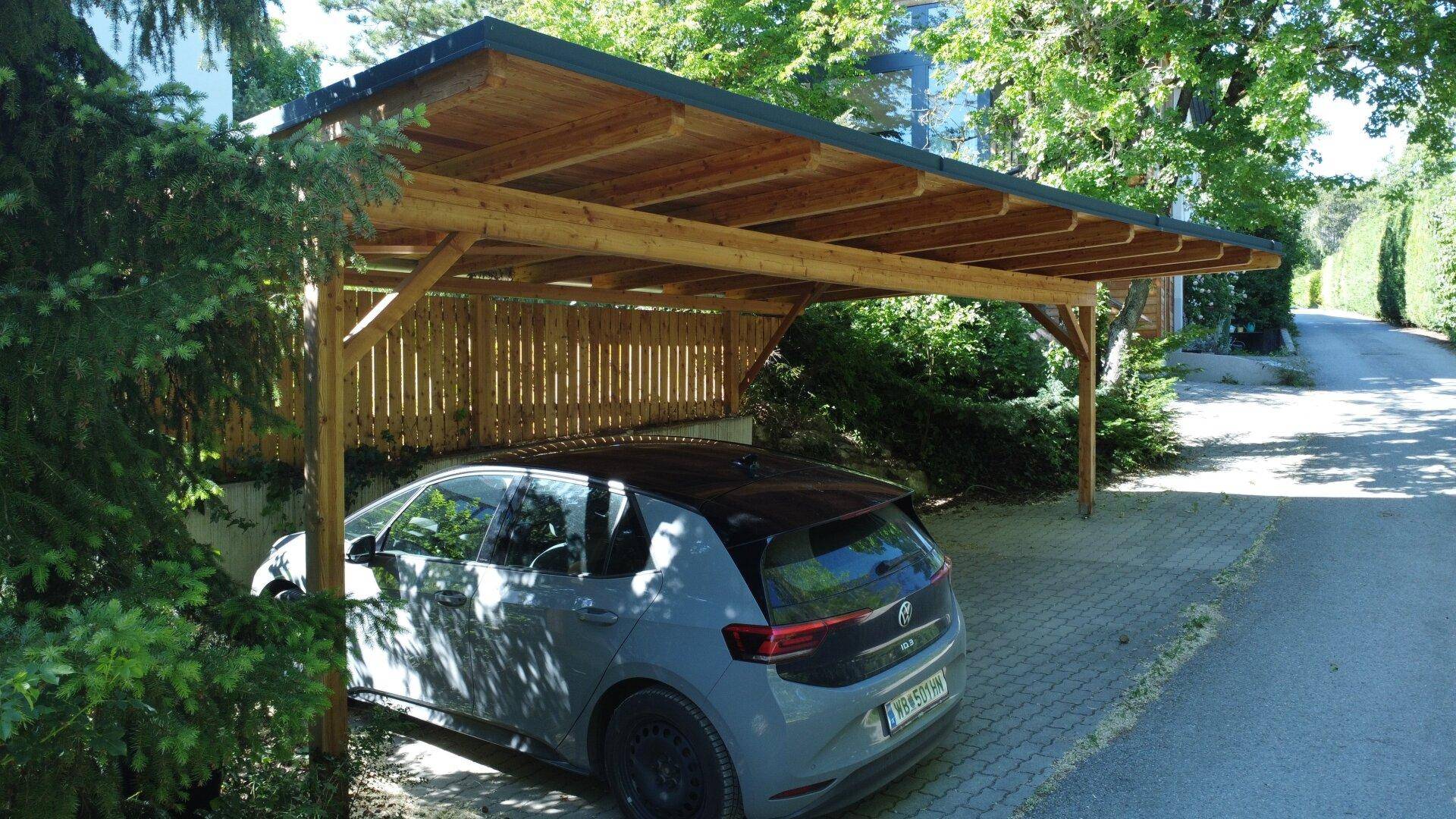 Holzcarport bietet geschützten Stellplatz für ein Fahrzeug auf gepflastertem Untergrund neben Bäumen.