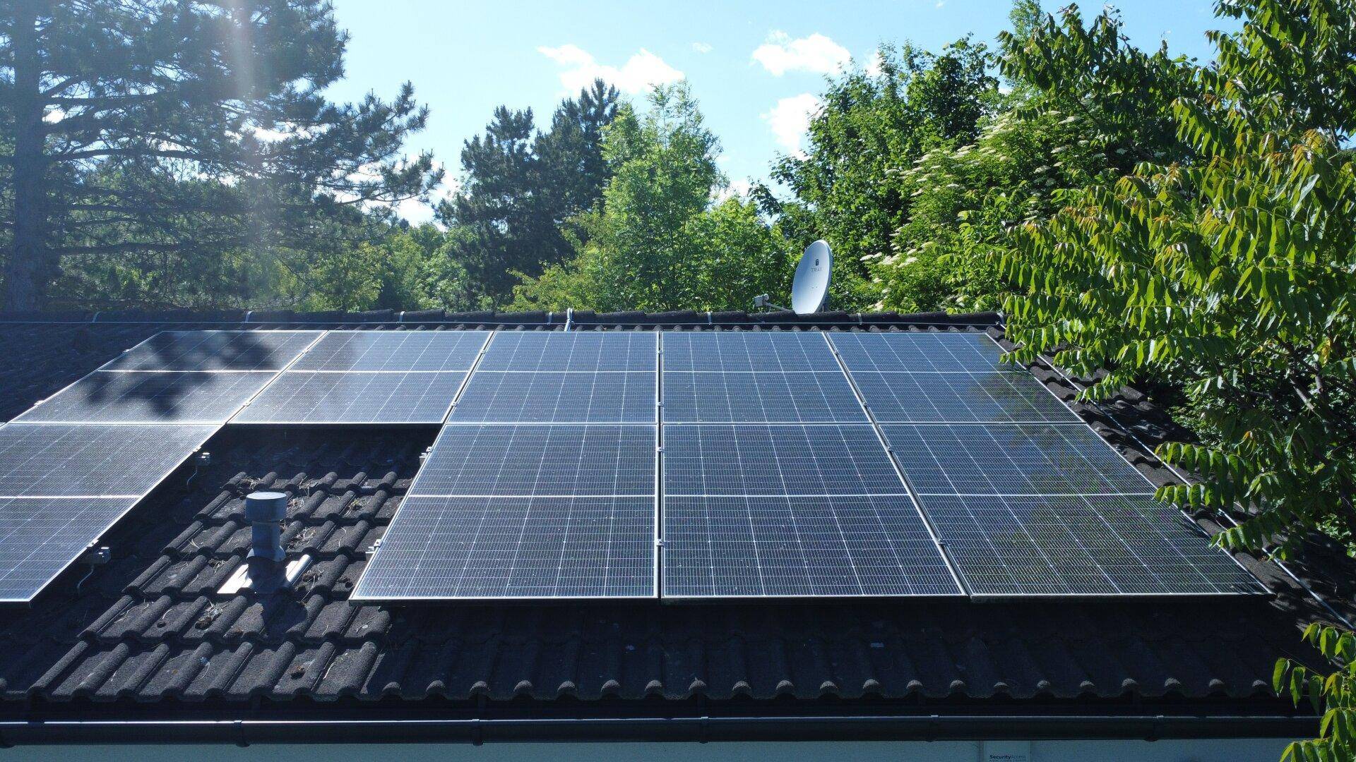 Dachfläche mit installierten Photovoltaikmodulen zur Energiegewinnung unter blauem Himmel und Bäumen.