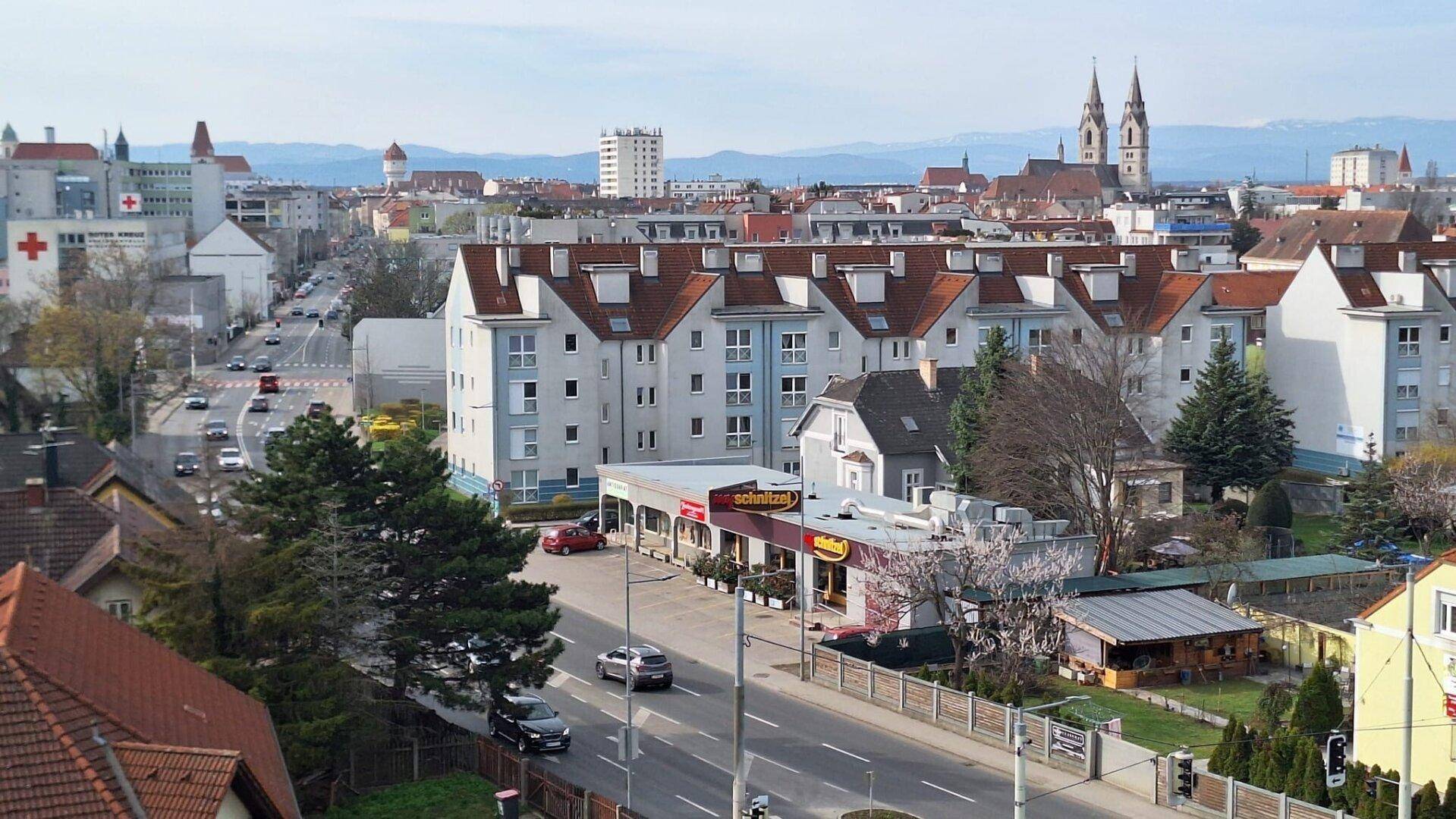 Panoramablick über eine Stadt mit Wohngebäuden, Geschäften und Bergen am Horizont.