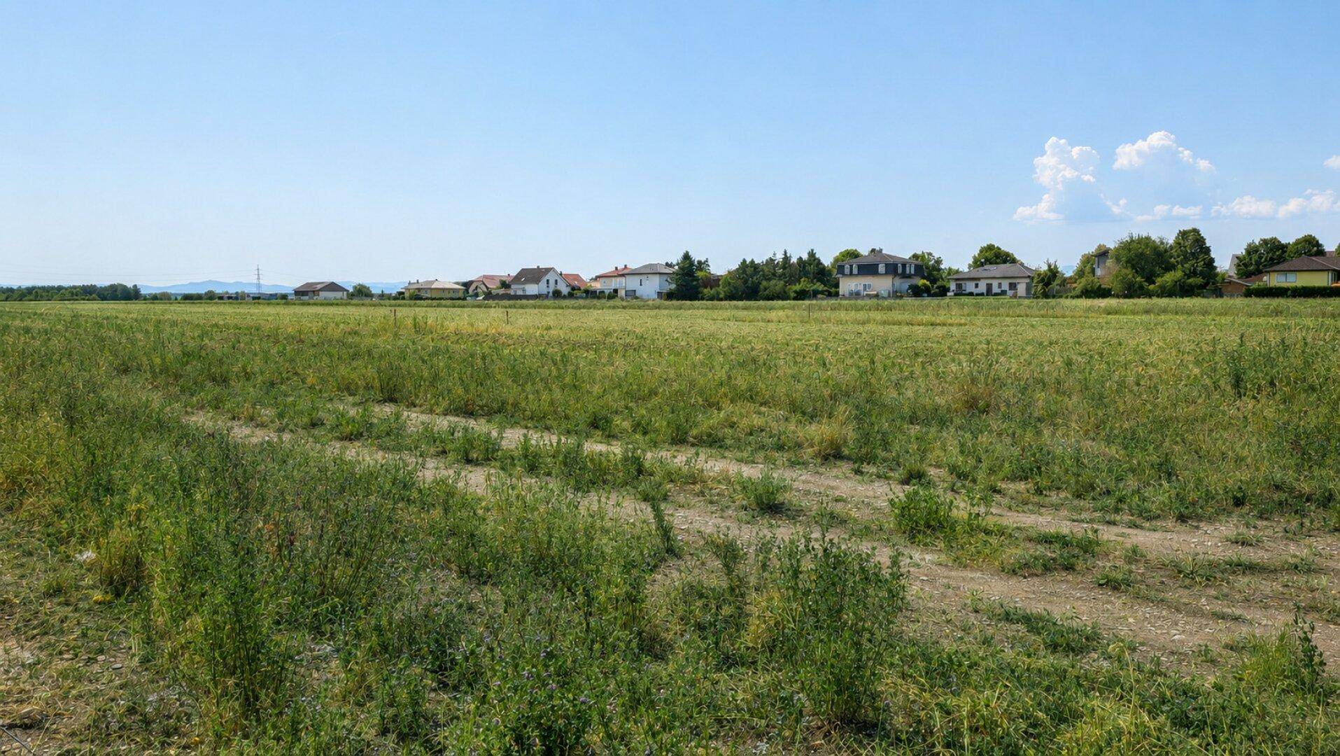 Offene Felder mit Häusern am Horizont und weitem Blick in die Landschaft.