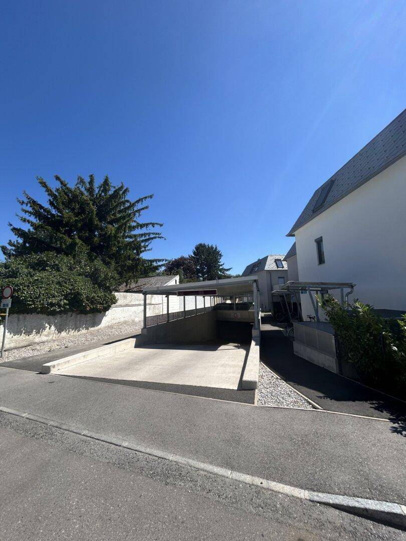 Zufahrt zur Tiefgarage eines modernen Gebäudes an einem sonnigen Tag, gut gepflegt.
