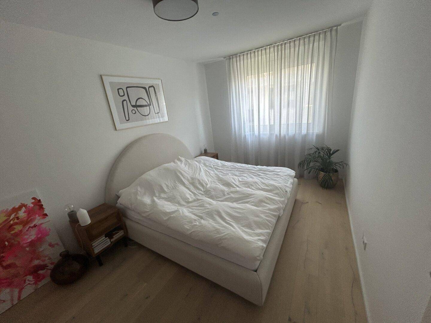 Helles Schlafzimmer mit Doppelbett, Holzboden und großem Fenster, das eine ruhige Atmosphäre schafft.