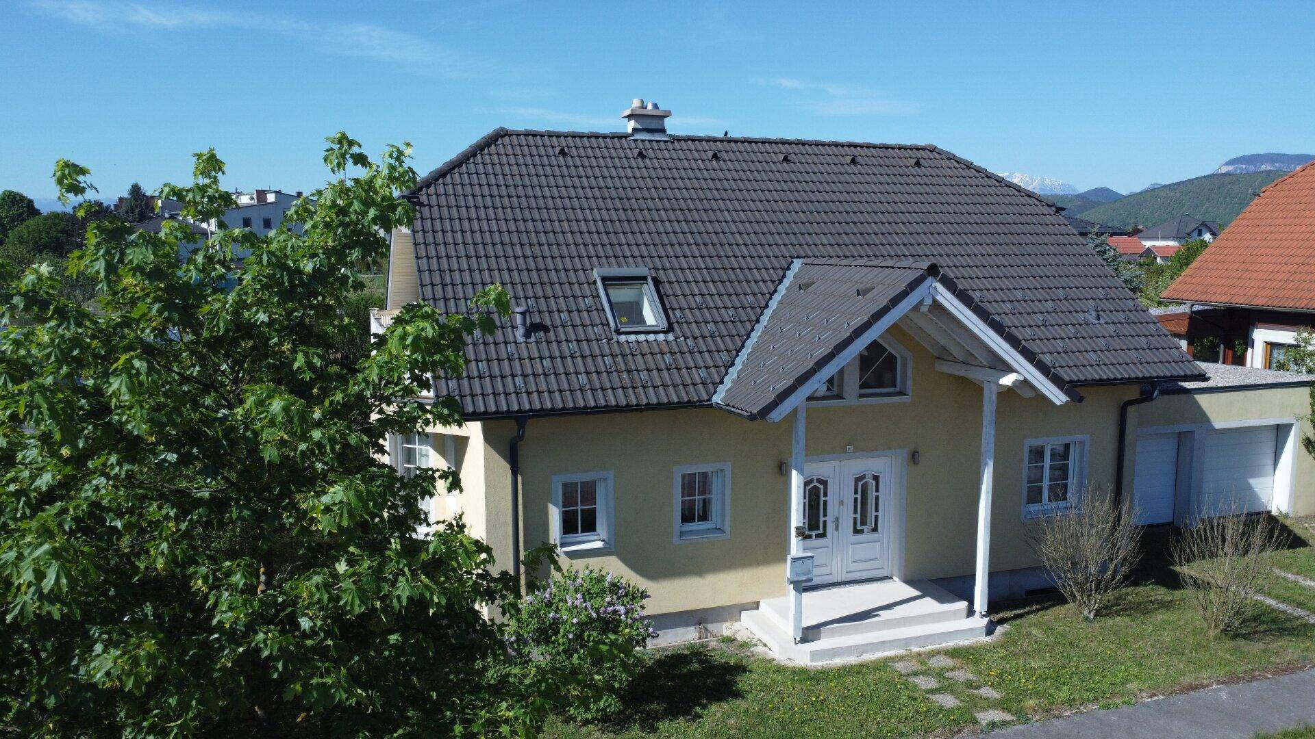 Ansicht des modernen Einfamilienhauses mit gelber Fassade, dunklem Dach und gepflegtem Vorgarten.