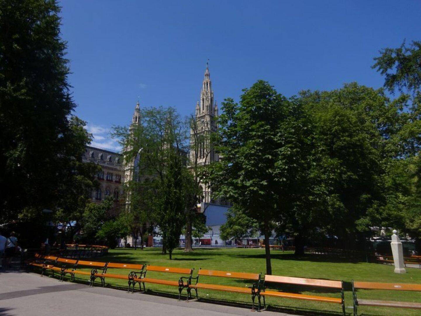 Weitläufiger Park mit grünen Rasenflächen, Bäumen und Bänken vor einem historischen Gebäude.