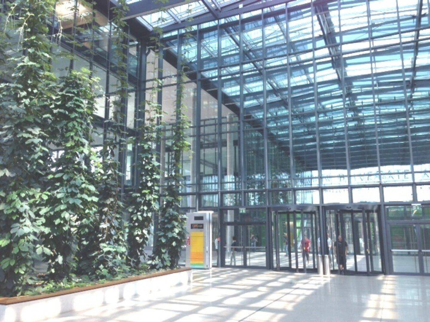 Helle, moderne Lobby mit hoher Glasfassade, viel Grün und drehbaren Eingangstüren für Besucher.