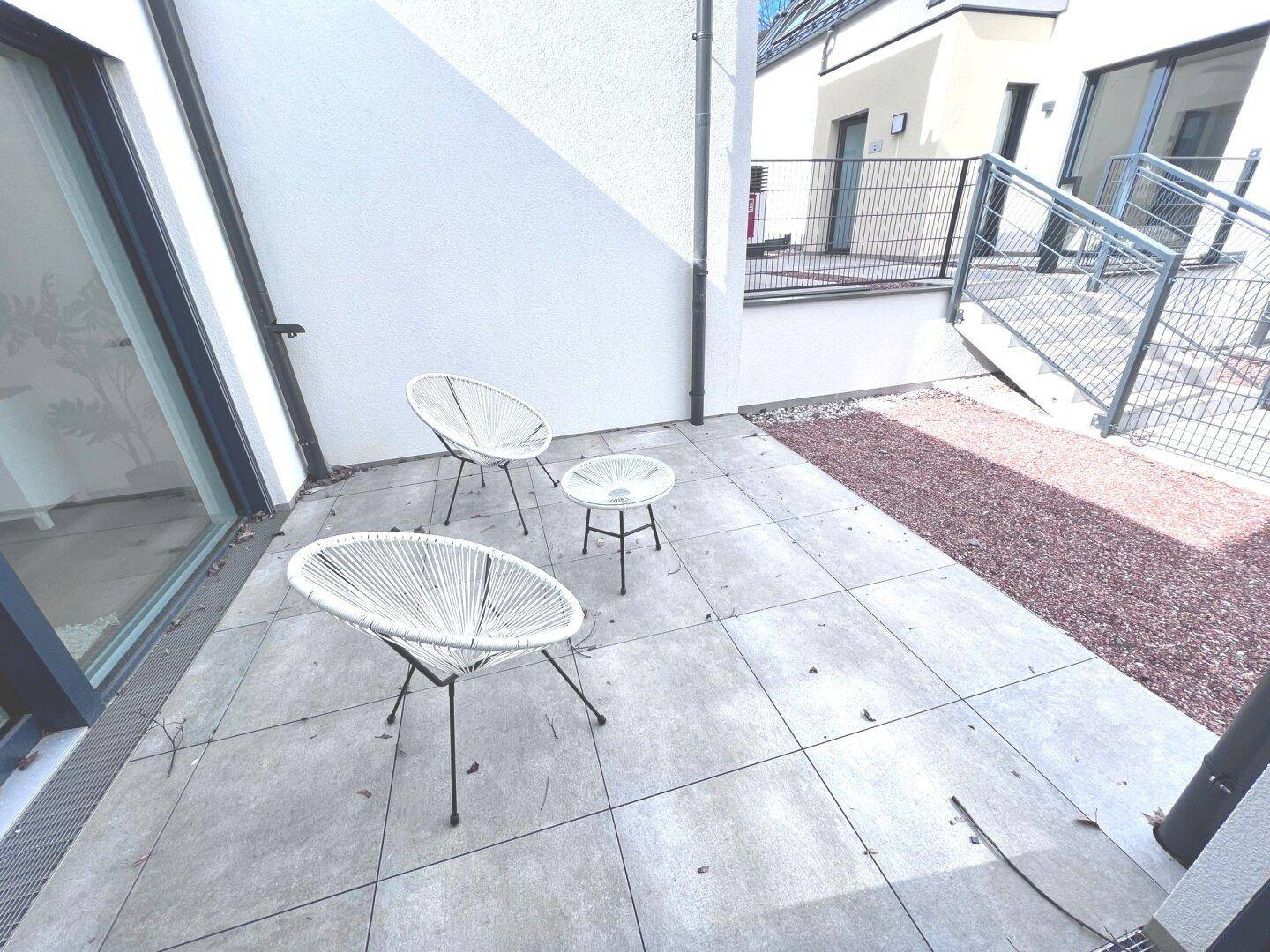 Gepflasterte Terrasse mit modernen Outdoor-Sesseln und einem kleinen Beistelltisch.