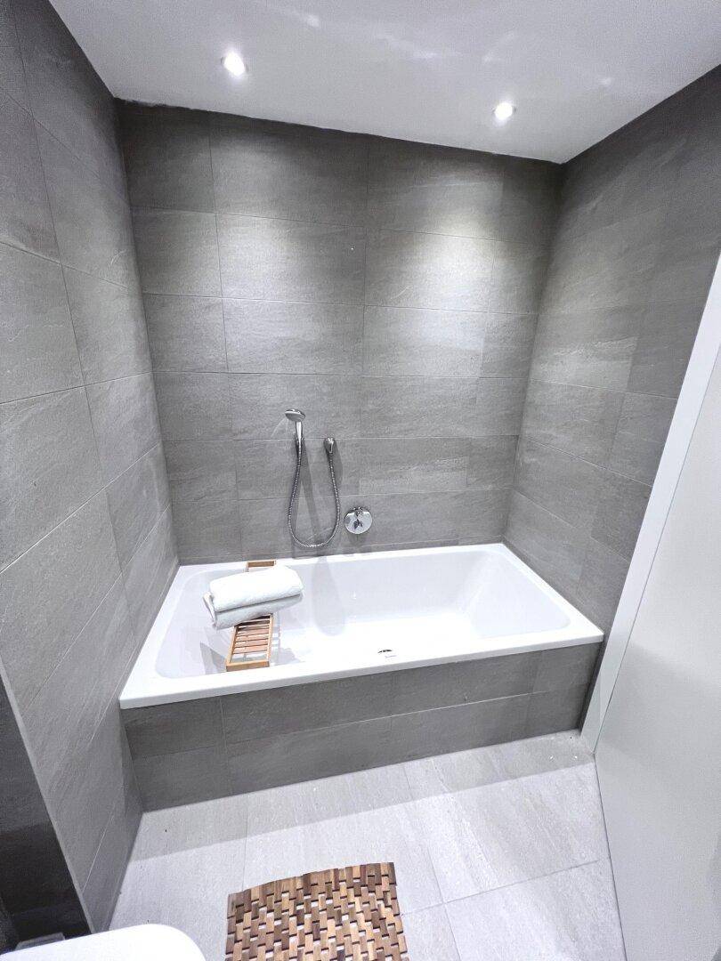 Modernes Badezimmer mit integrierter Badewanne und grauen Fliesen an Wänden und Boden.