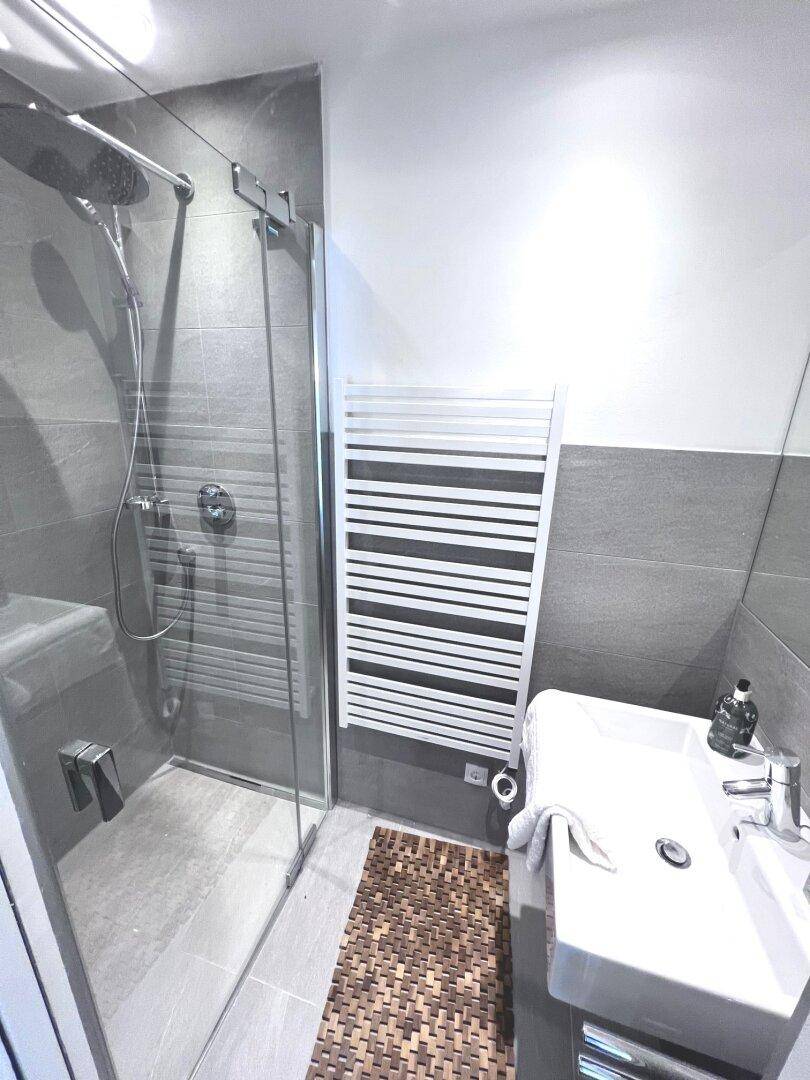 Helles Badezimmer mit ebenerdiger Dusche, modernem Waschbecken und grauen Fliesen.