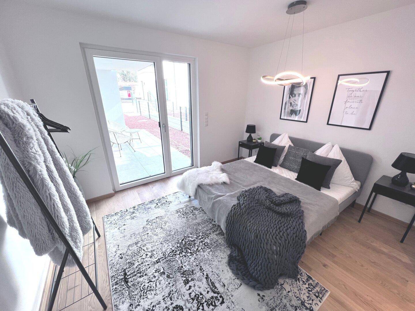 Helles Schlafzimmer mit modernem Bett, Nachttischen und großem Fenster mit Terrassenzugang.