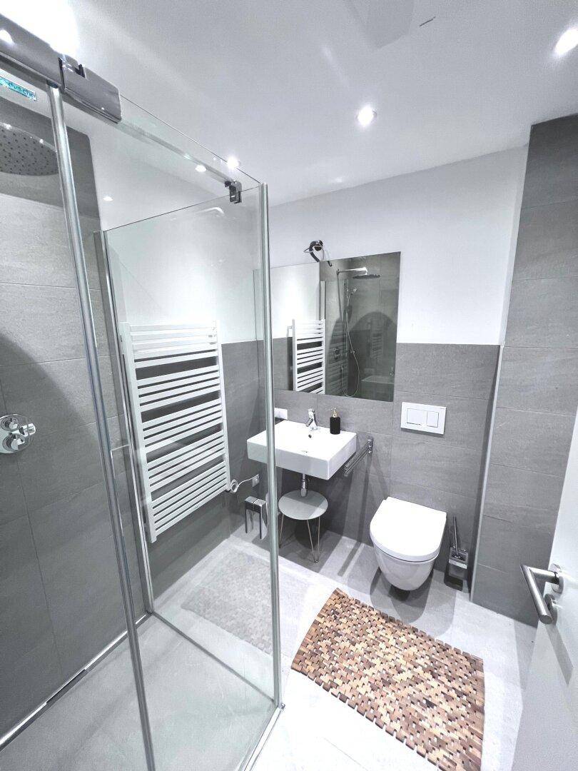 Modernes Badezimmer mit ebenerdiger Dusche, Wand-WC und beheiztem Handtuchhalter.