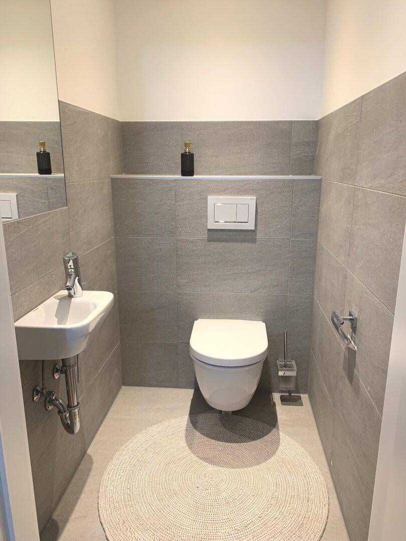 Modernes Gäste-WC mit kleinem Waschbecken und Wand-WC in neutralen Grautönen.