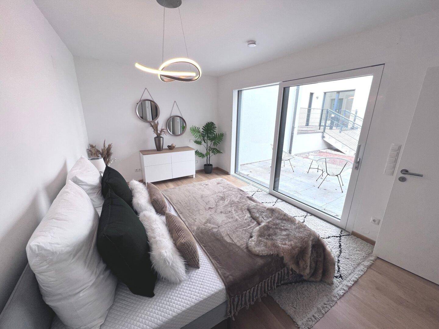 Helles Schlafzimmer mit gemütlichem Bett und großem Fenster mit Zugang zur Terrasse.