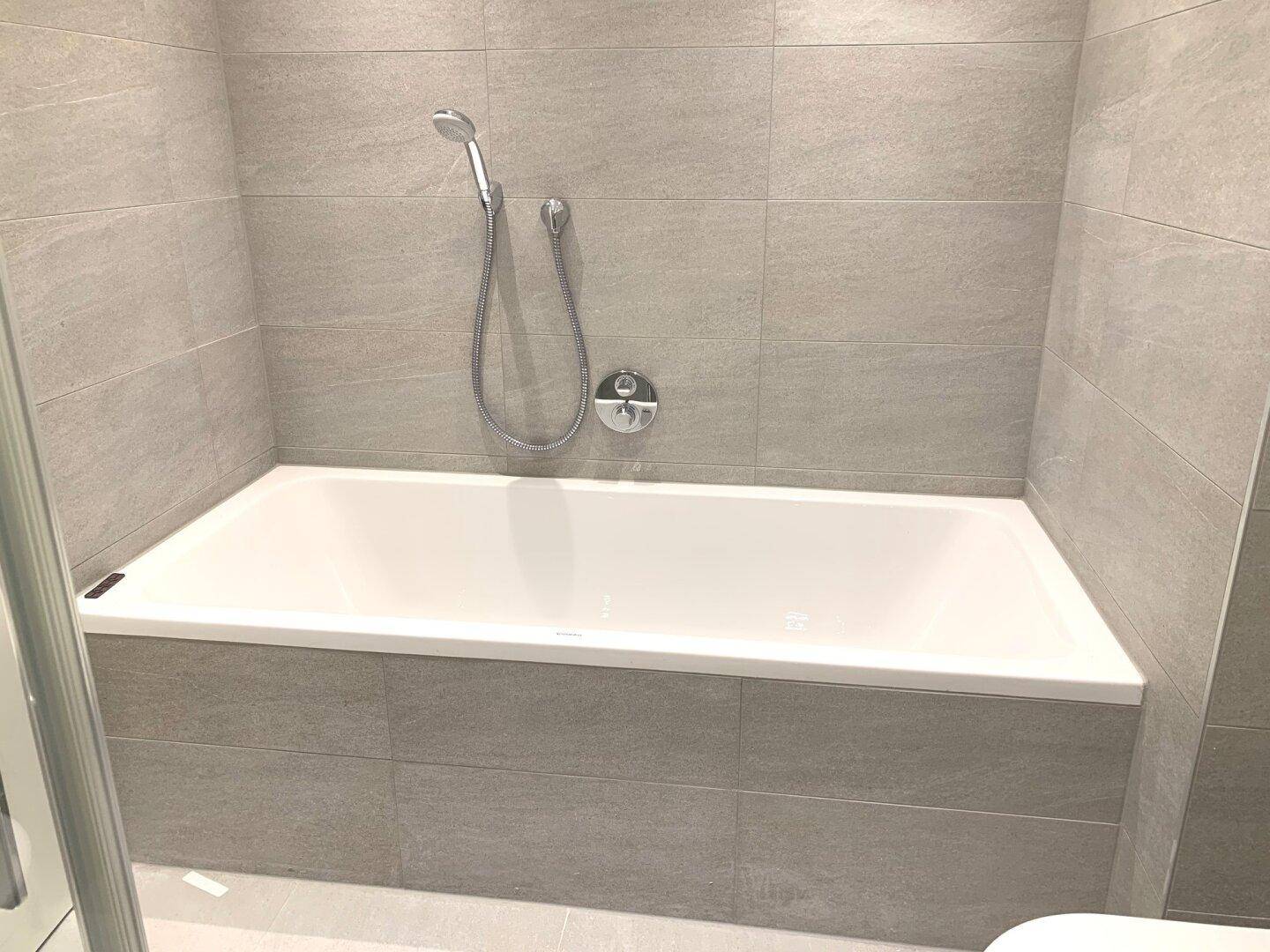 Modernes Badezimmer mit grauen Fliesen und einer eingebauten Badewanne.