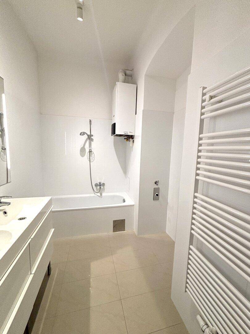 Helles Badezimmer mit Badewanne, Doppelwaschbecken und beheiztem Handtuchhalter.