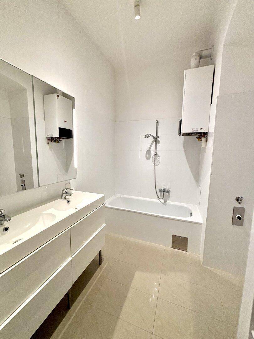 Modernes Badezimmer mit Doppelwaschbecken, Badewanne und hellen Fliesen.