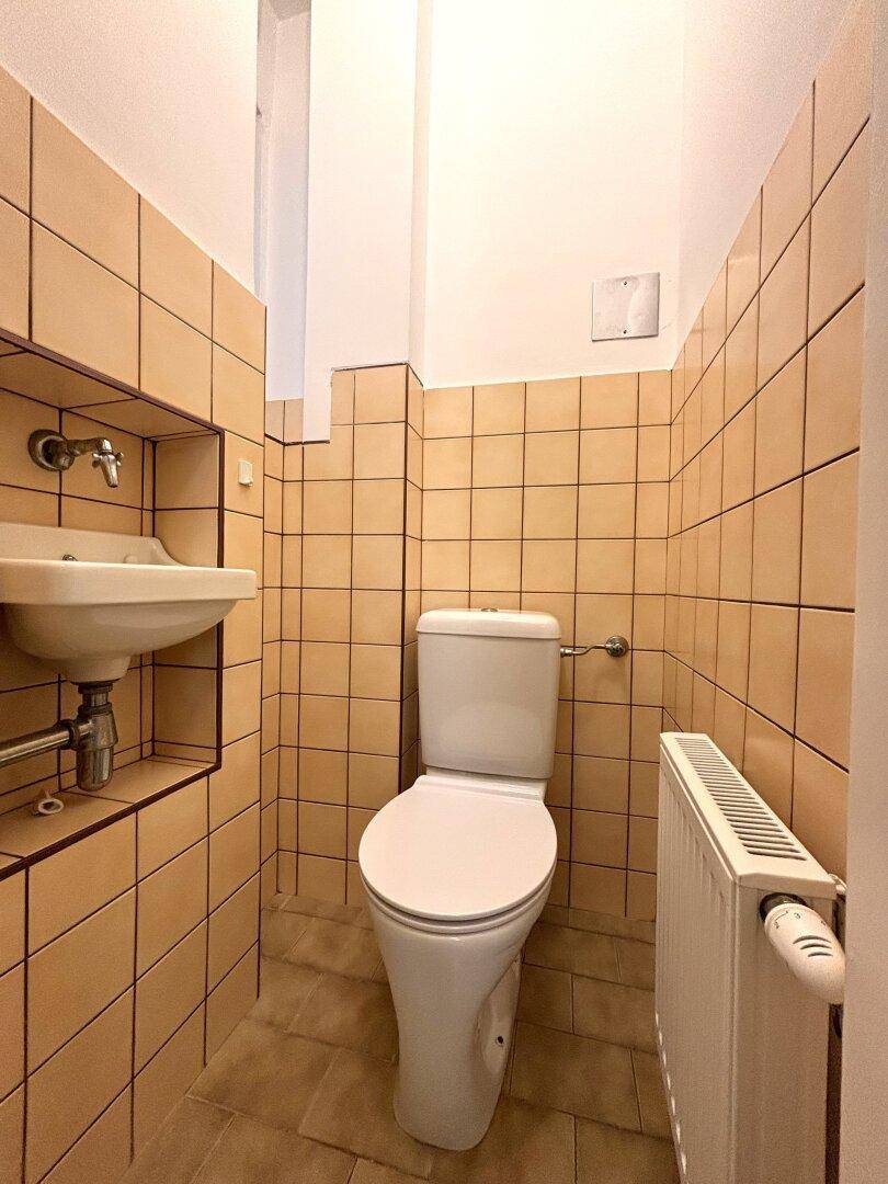 Kleines Gäste-WC mit beigen Fliesen, Toilette und kleinem Waschbecken.