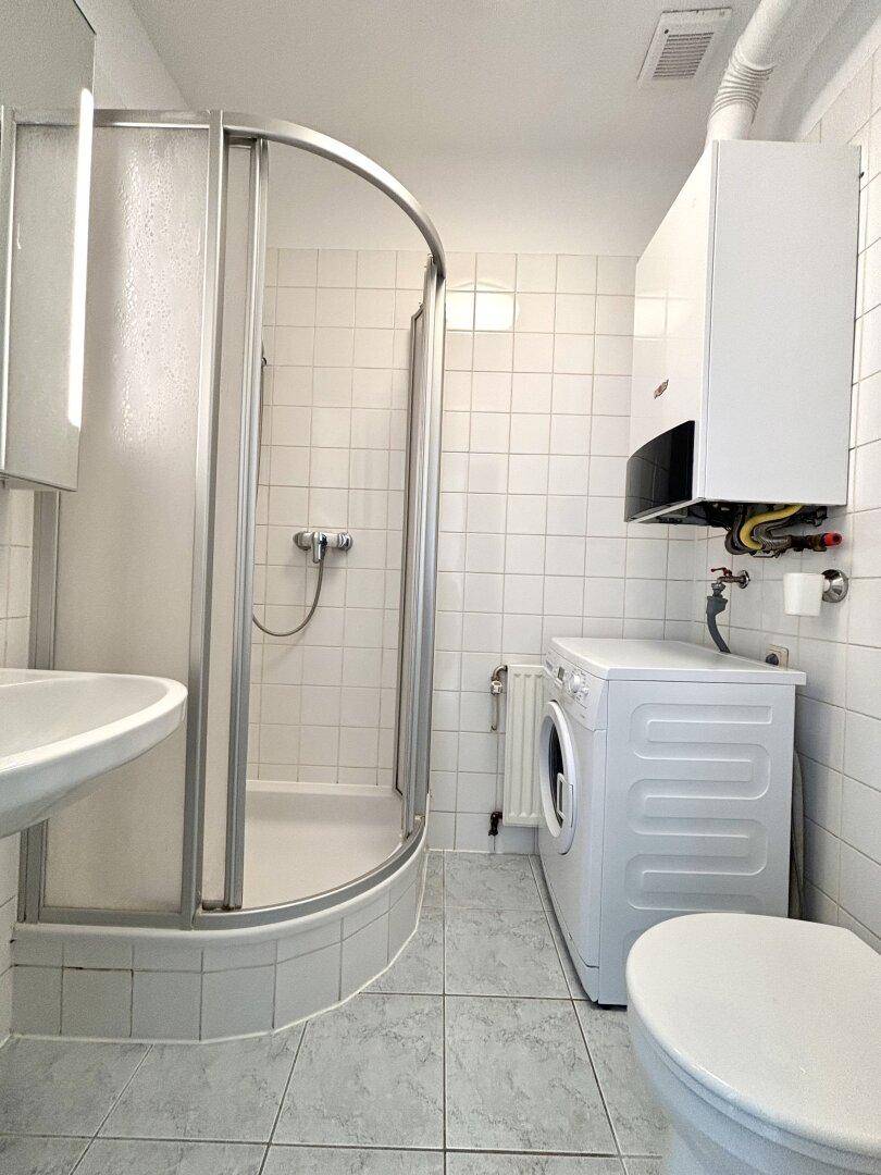 Funktionales Badezimmer mit Duschkabine, Waschmaschine und Gastherme an der Wand.