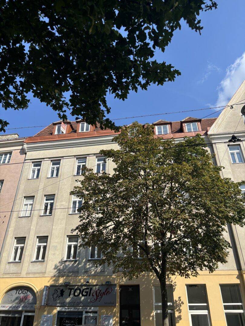 Historische Fassade eines Mehrfamilienhauses mit Mansarddach und Geschäften im Erdgeschoss.