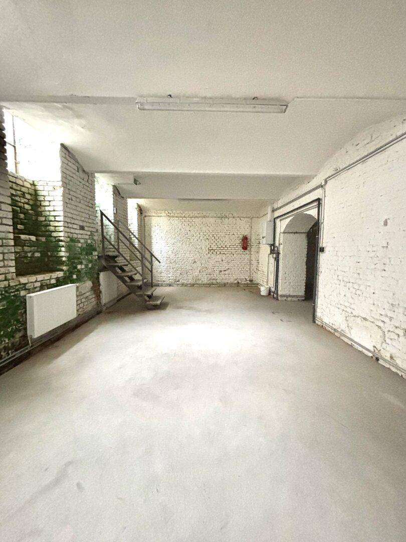 Geräumiger Kellerraum mit weiß gestrichenen Ziegelwänden, Betonboden, gewölbter Decke und einer Metalltreppe.