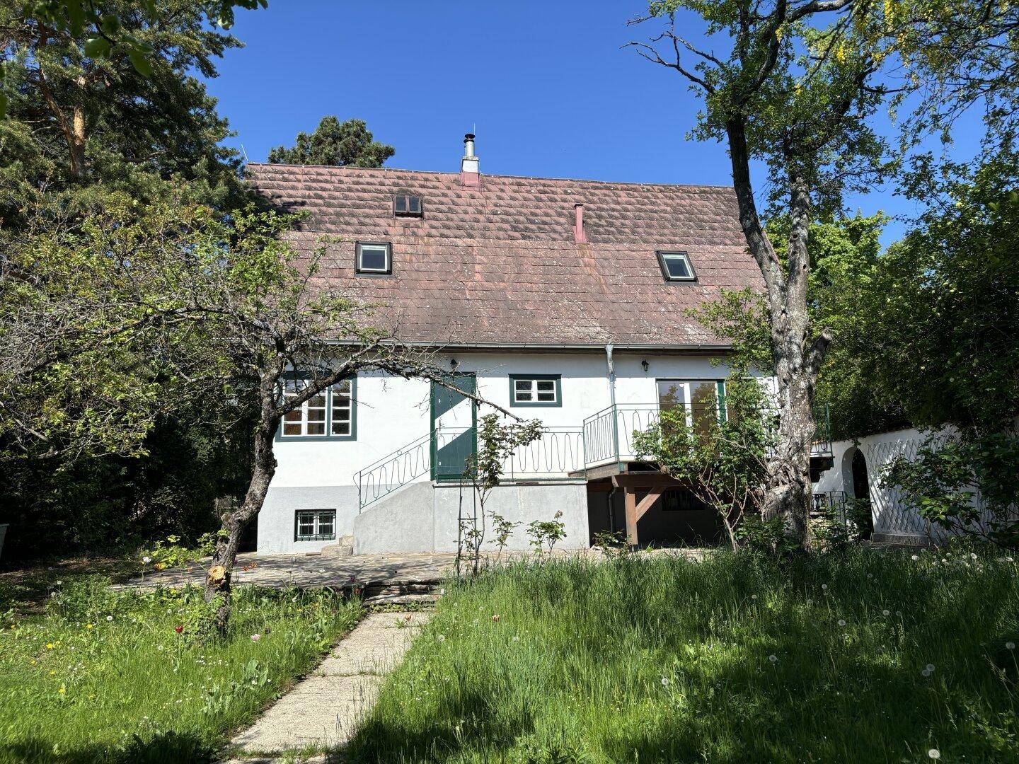 Charmantes Landhaus mit rotem Ziegeldach, umgeben von üppigem Grün und Bäumen.